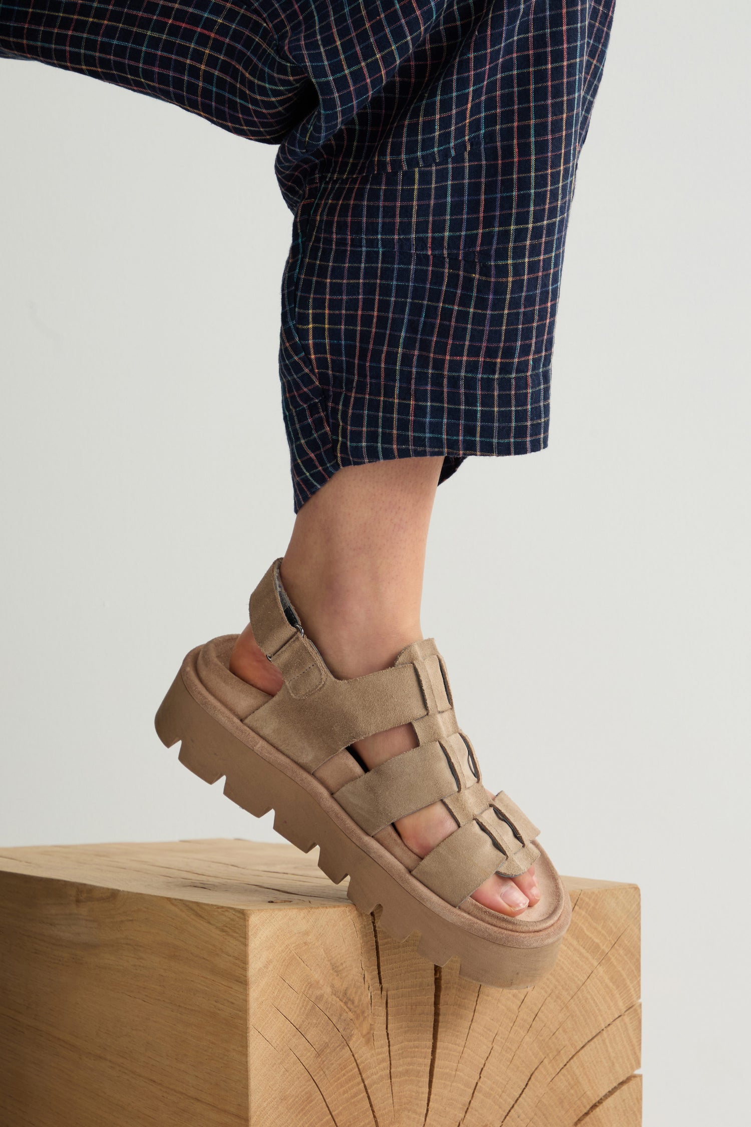 A person wearing checkered pants and Suede Platform Velcro Sandals by Lofina stands confidently on a wooden block.