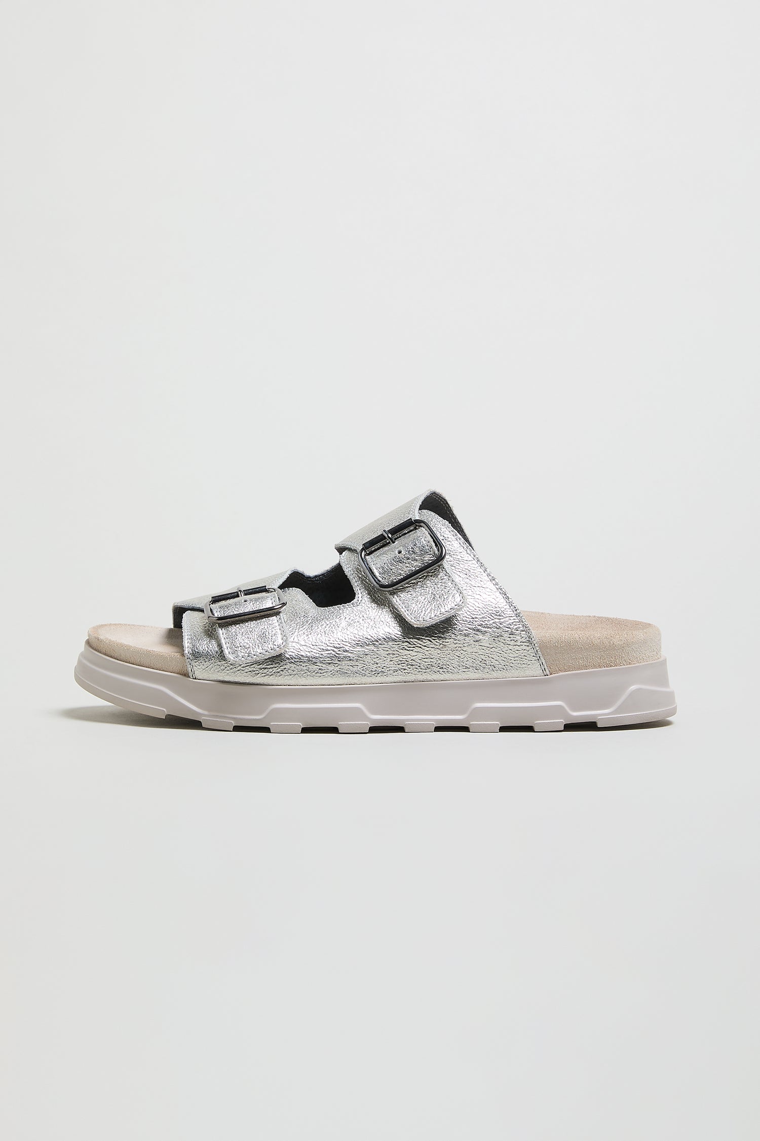 The Double Buckle Leather Sliders in metallic silver feature two adjustable straps and a cushioned sole, shown on a plain white background.