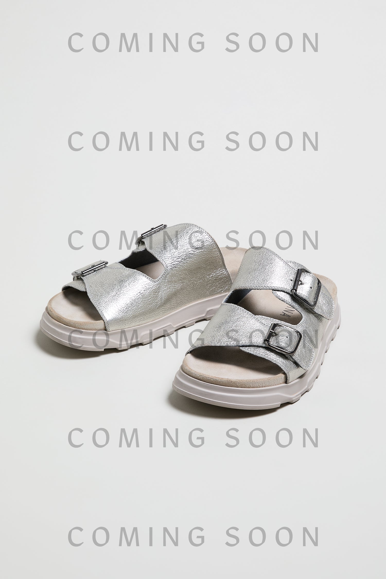 A pair of metallic silver Double Buckle Leather Sliders (style LOFI1E240) is shown on a white background, overlaid with repeated “COMING SOON” text.