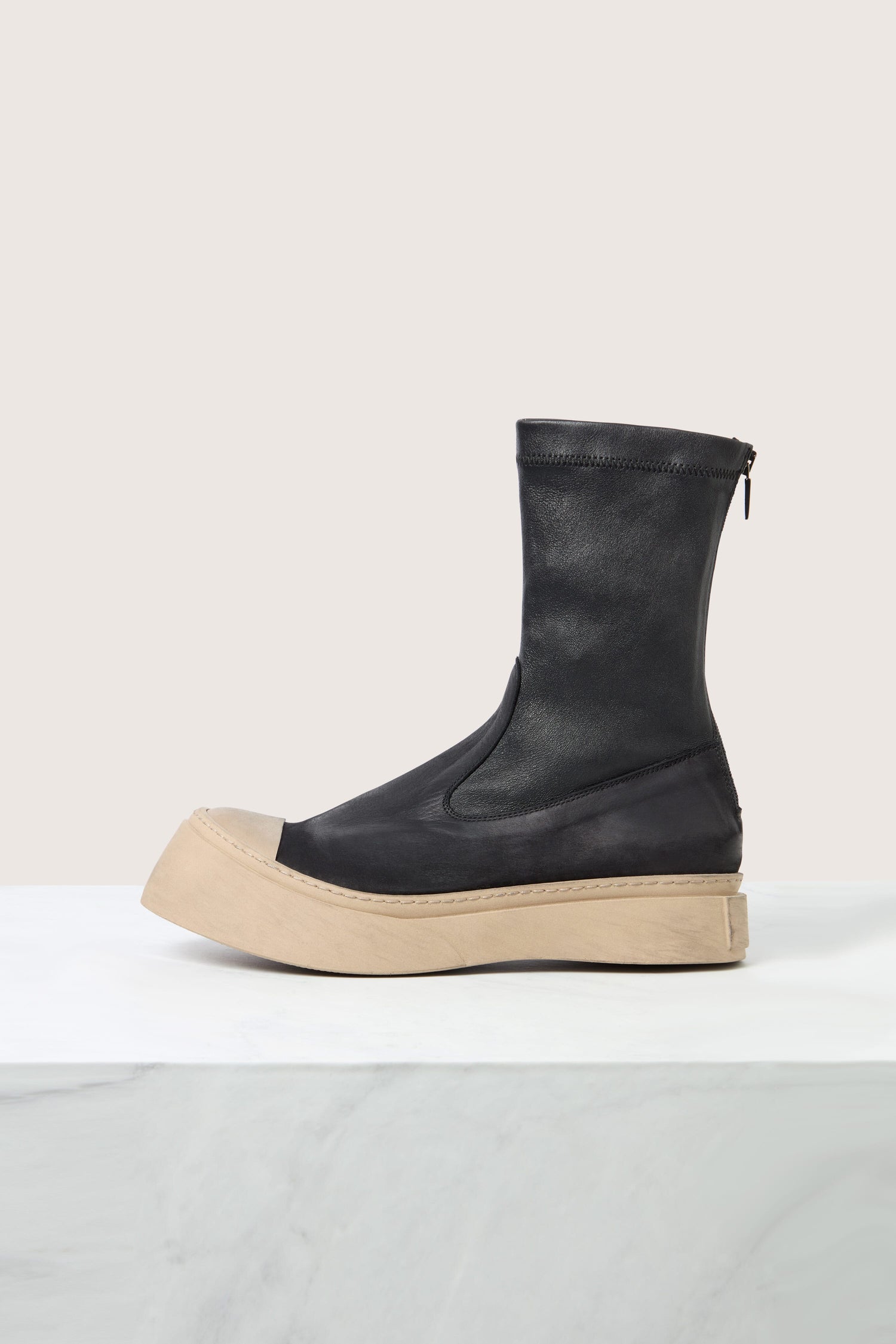 The Contrast Leather Stretch Boot, made from ultra-soft calfskin and featuring a beige rubber sole and a zipper on the back, is displayed on a white surface against a light-colored background.