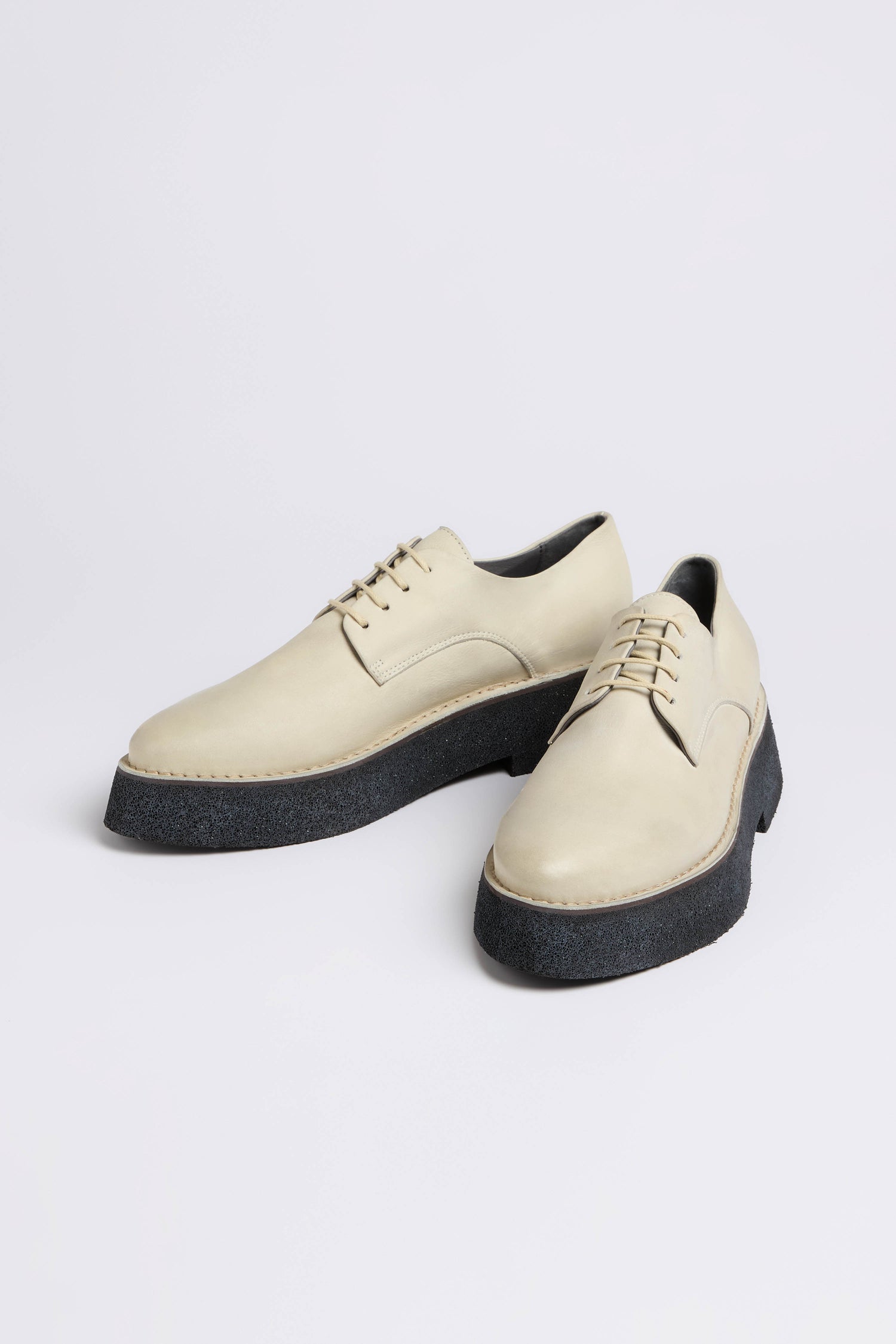 These cream-colored lace-up shoes, handcrafted in Italy, feature thick black soles on a white background. The Lace Up Leather Brogues boast a contemporary platform sole that seamlessly blends style with sophistication.