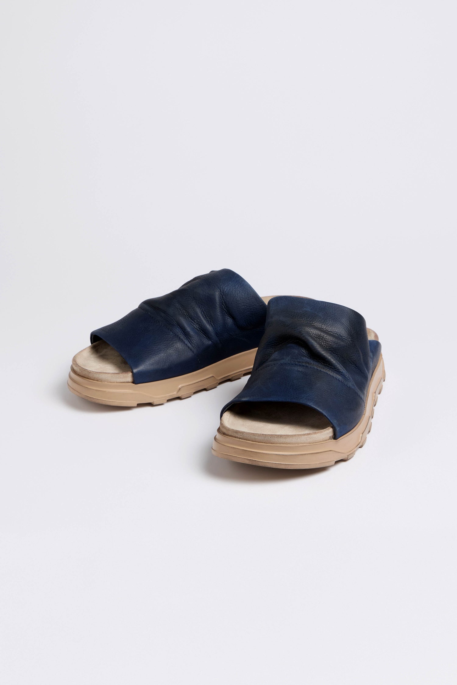 The Navy Crushed Leather Sliders, featuring cushioned soles and beige accents, epitomize effortless luxury in dark blue leather, photographed front-facing on a plain background.