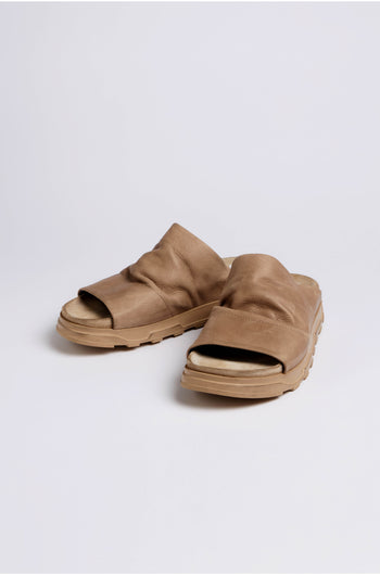 The Crushed Leather Sliders, a pair of tan slip-on sandals with thick soles, are shown on a plain white background. Style LOFI3364 from SS26 offers comfortable versatility for everyday wear.