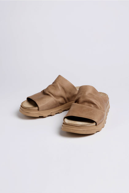 The Crushed Leather Sliders, a pair of tan slip-on sandals with thick soles, are shown on a plain white background. Style LOFI3364 from SS26 offers comfortable versatility for everyday wear.