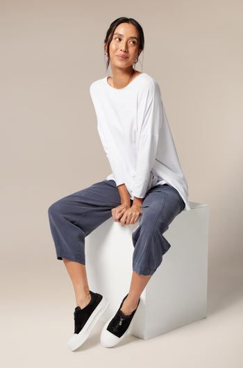 A woman is sitting on a cube wearing Zip Detail Suede Pumps and a minimalist style white t-shirt and cropped pants.