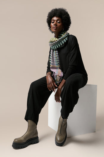 An elegant black woman with Platform Zip Front Leather Boots, wearing a stylish scarf, sits gracefully on a white cube.