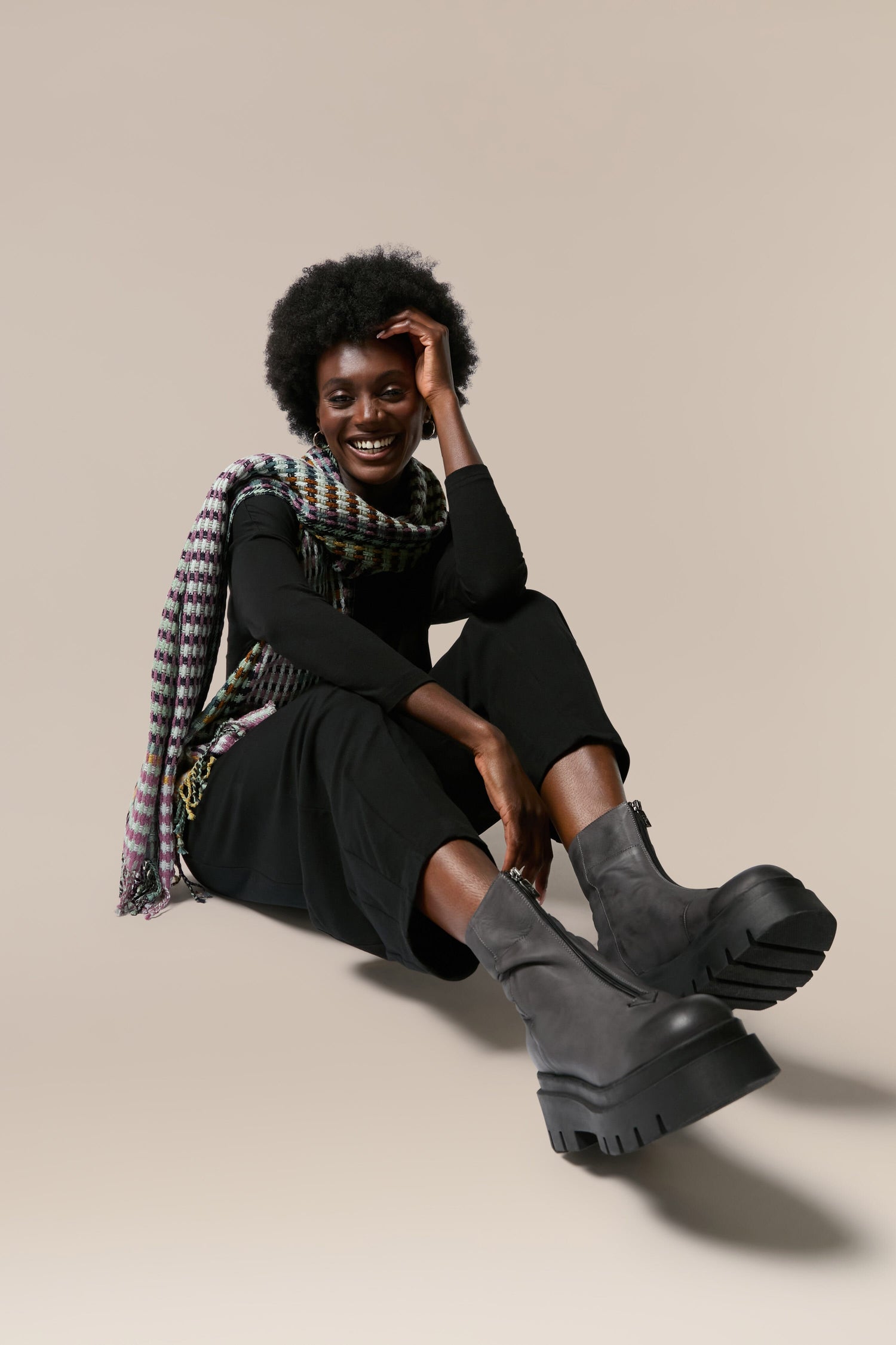 A black woman sitting on the ground in a scarf, wearing Platform Zip Front Leather Boots.