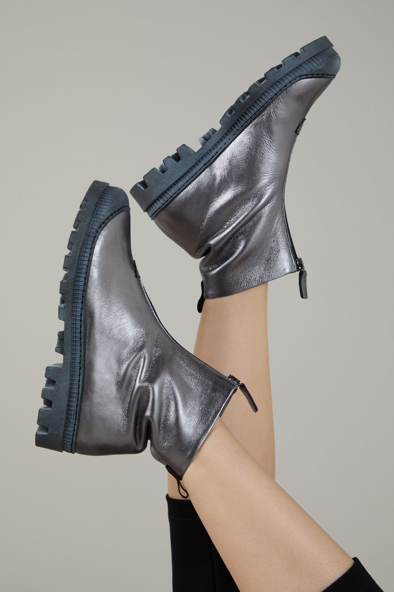 Two legs raised in the air, wearing Gunmetal Zip Front Leather Boots with chunky soles, set against a plain light background.