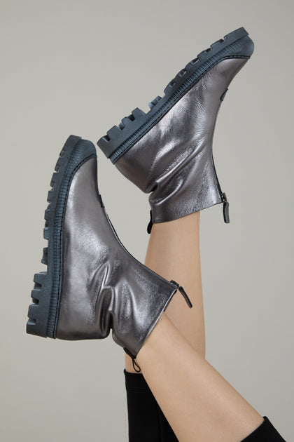 Two legs raised in the air, wearing Gunmetal Zip Front Leather Boots with chunky soles, set against a plain light background.