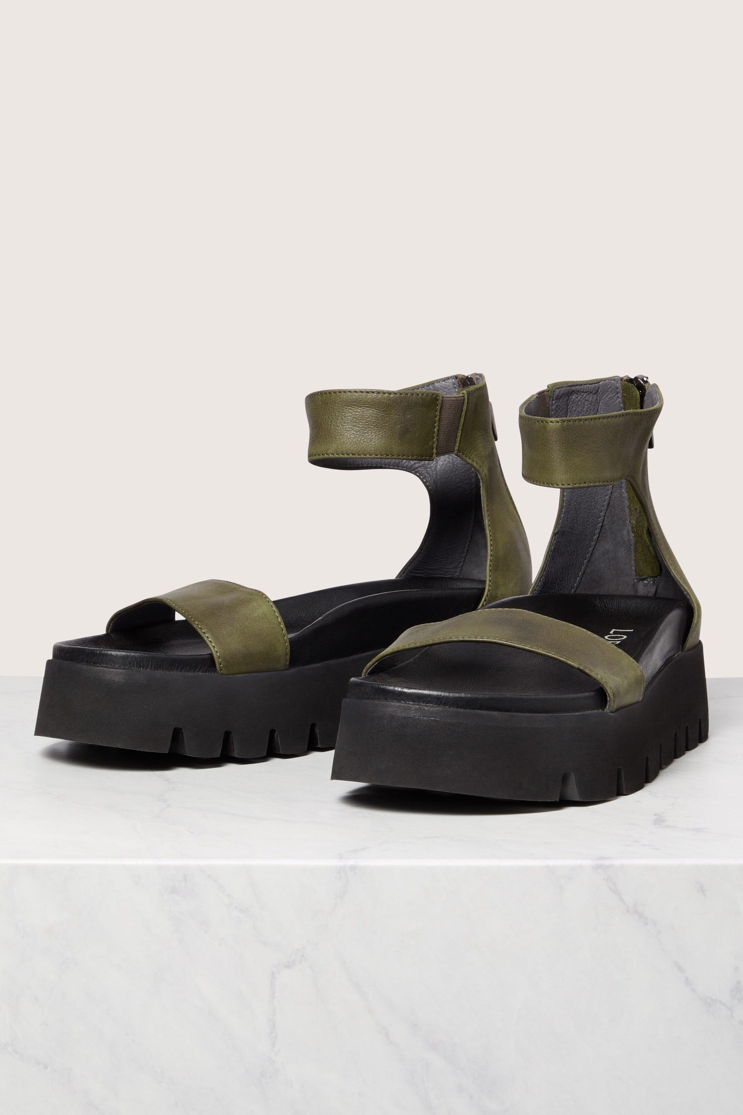 A pair of modern black Leather Platform Zip Sandals with green straps on a marble surface, showcasing Scandinavian design.