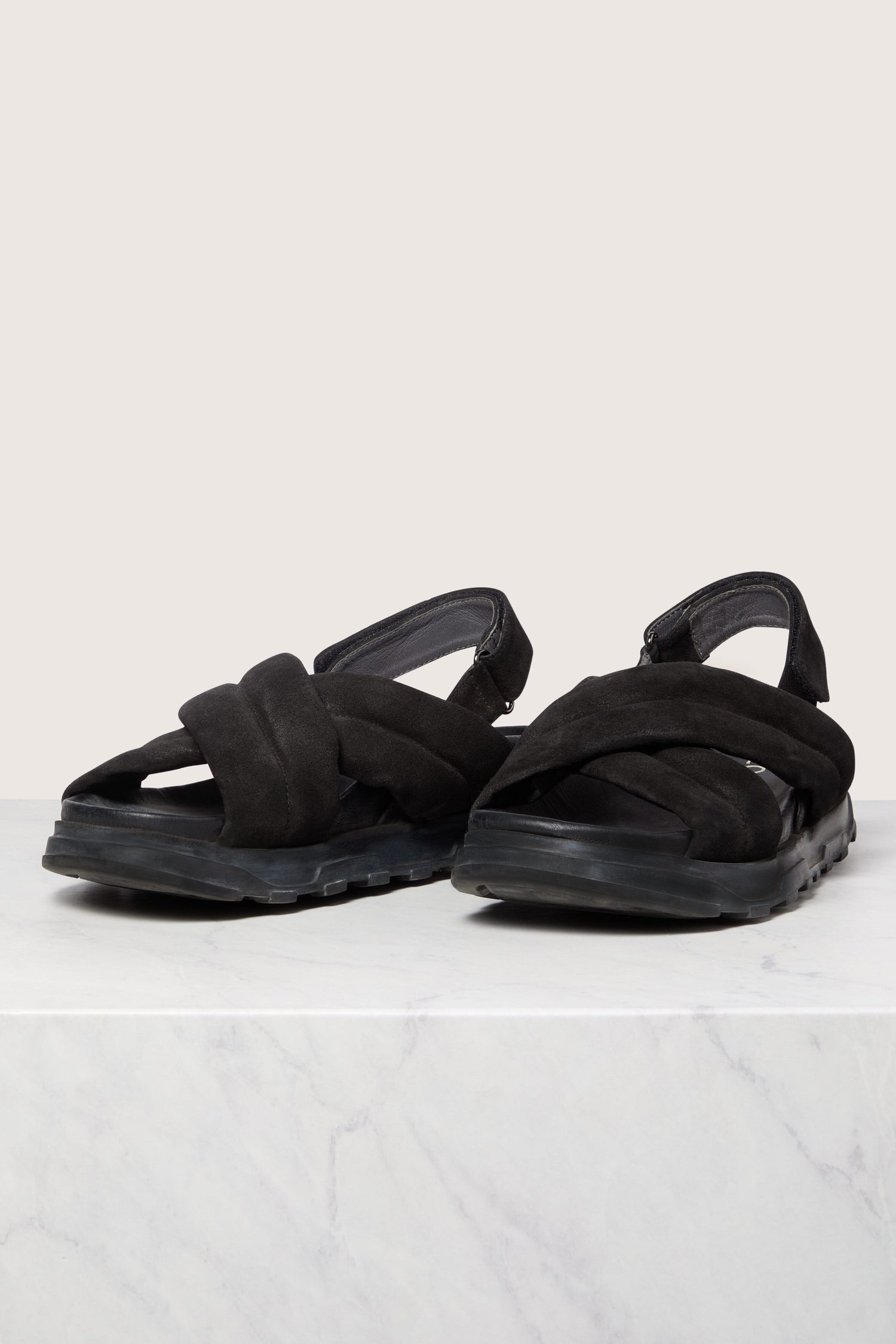 A pair of black, Suede Crossover Sandals with thick straps on a marble surface.