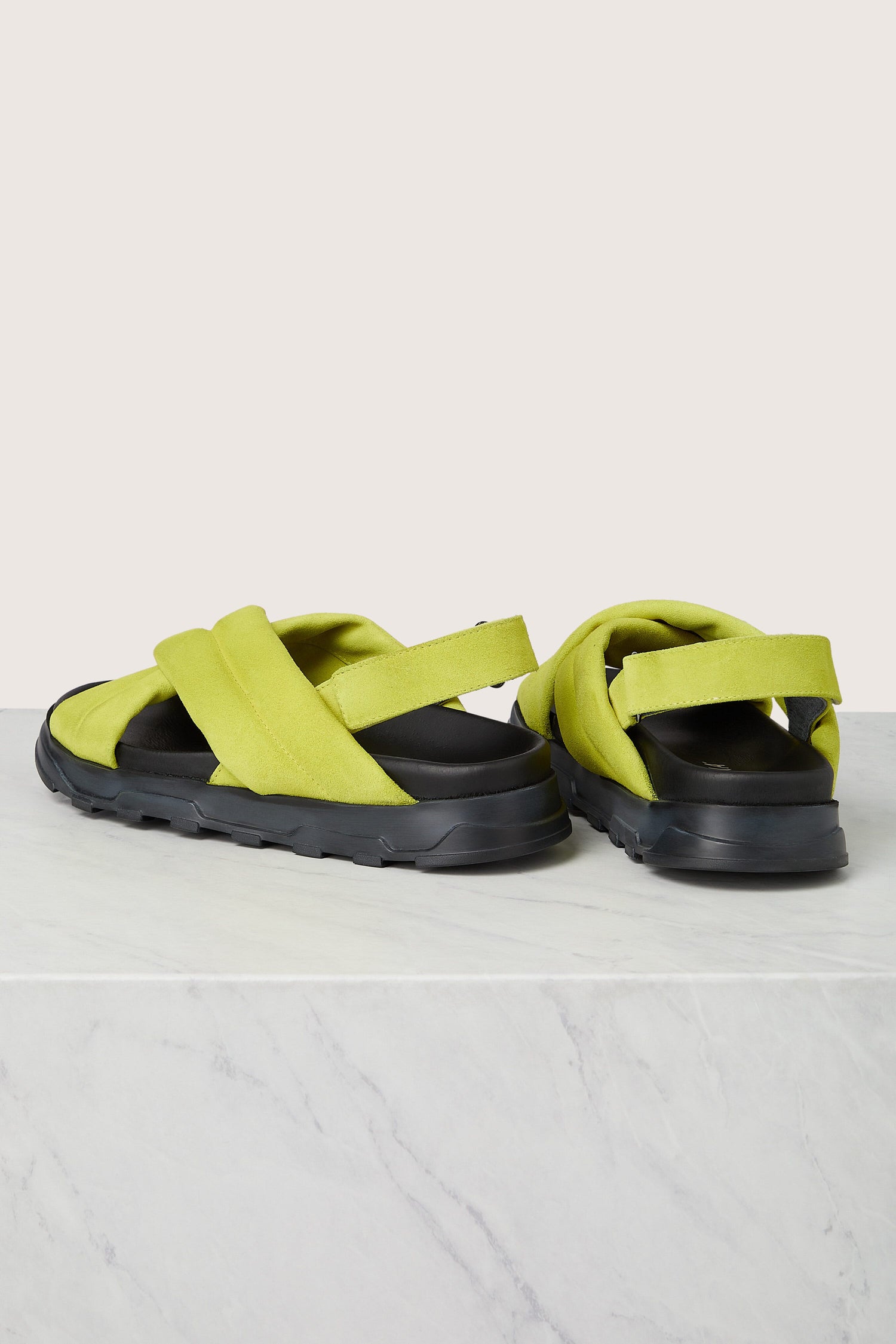 A pair of Modern Lime Green and Black Suede Crossover Sandals displayed on a marble surface featuring a durable sole.