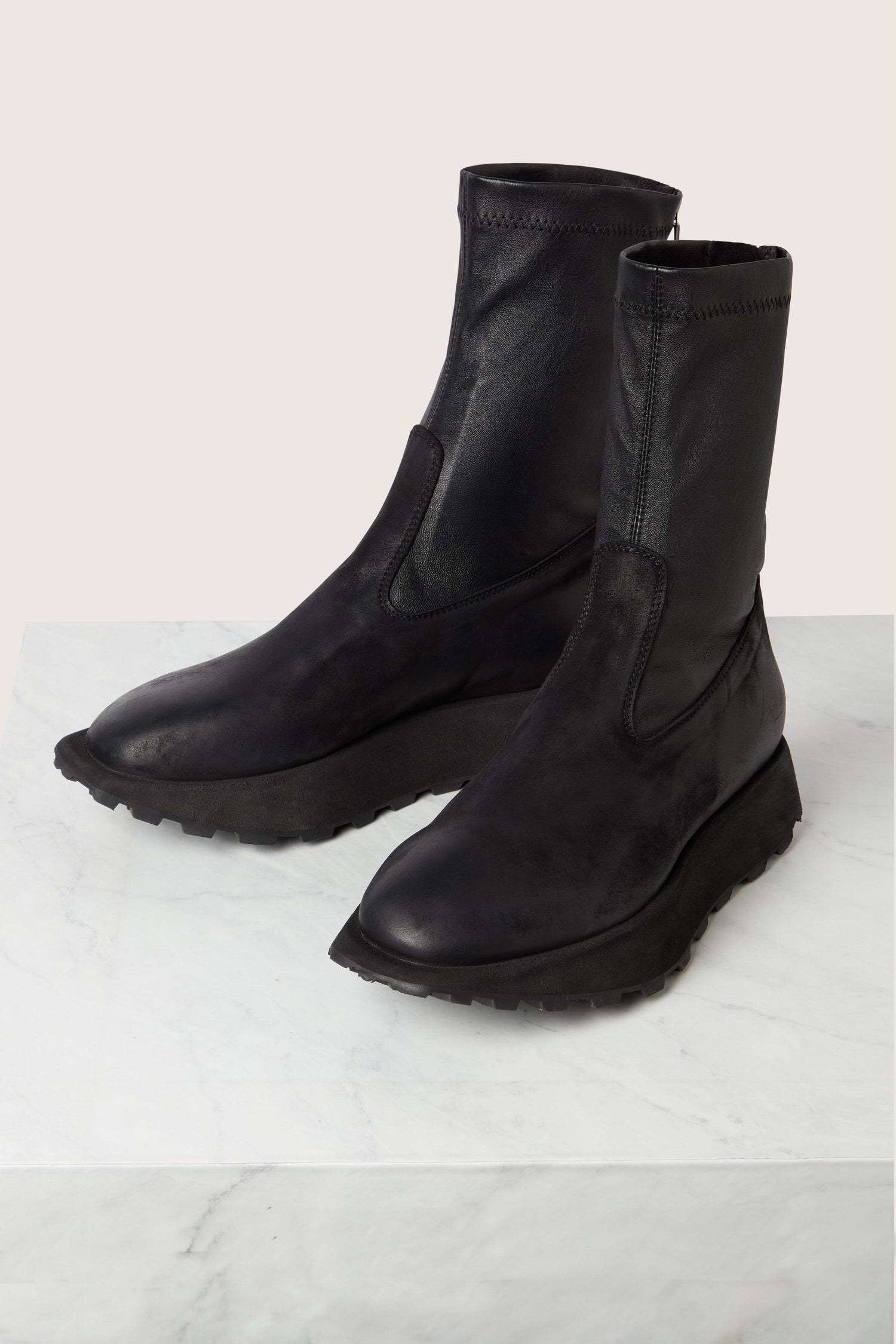 A pair of Leather Stretch Boots in black leather with a rugged sole, displayed on a white marble surface.