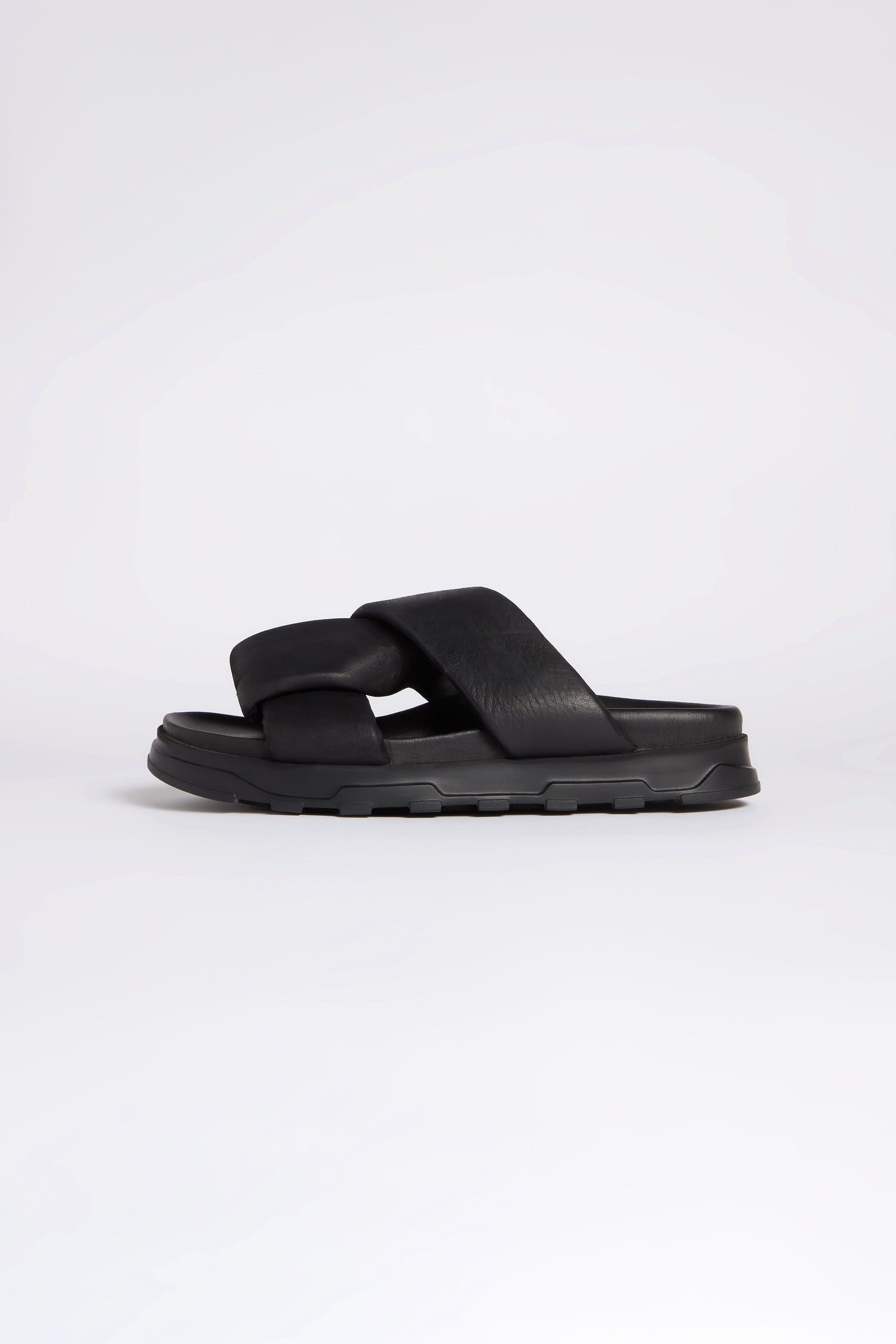 The Lattice Leather Sliders are black slip-on sandals with thick calfskin leather crisscross straps and a chunky sole, side view—a perfect choice for lovers of contemporary style.