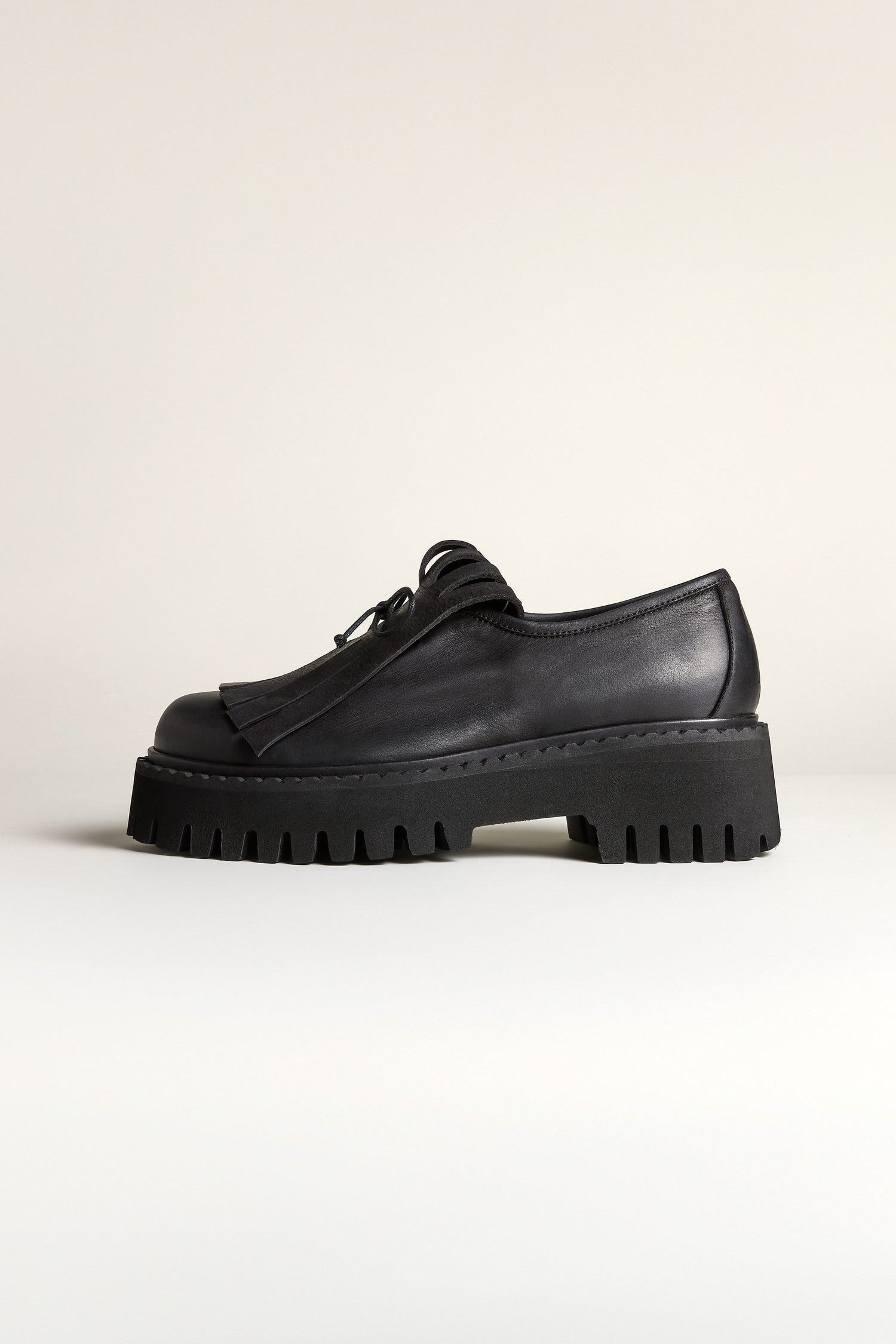The Fringe Top Leather Brogues in black showcase a handcrafted leather design with a thick, chunky sole and lace-up front, viewed from the side against a plain background—an elevated classic.