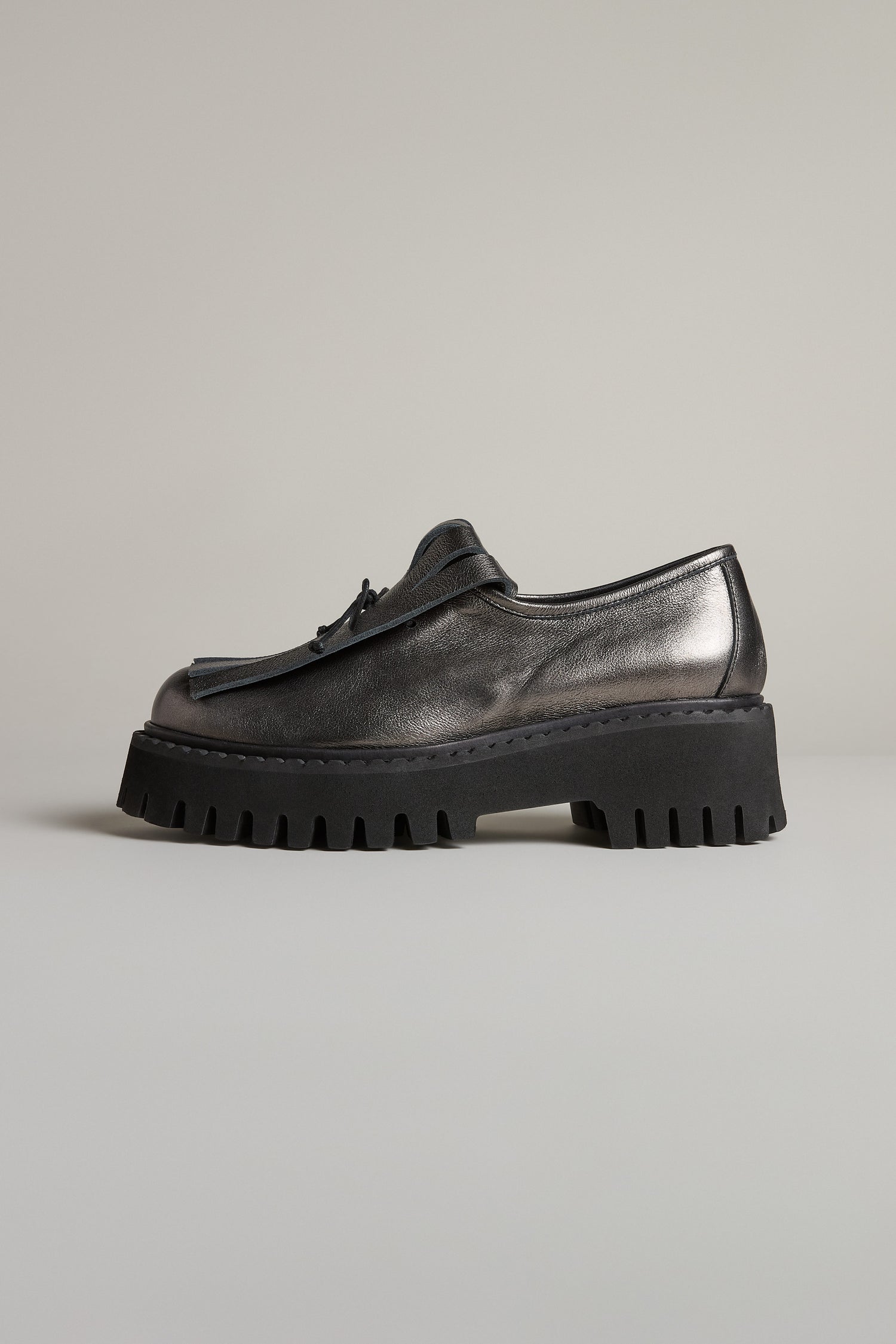 The Fringe Top Leather Brogues by Lofina, in black metallic leather with a chunky ridged sole, are showcased against a neutral background—an elegant twist on handcrafted shoes.