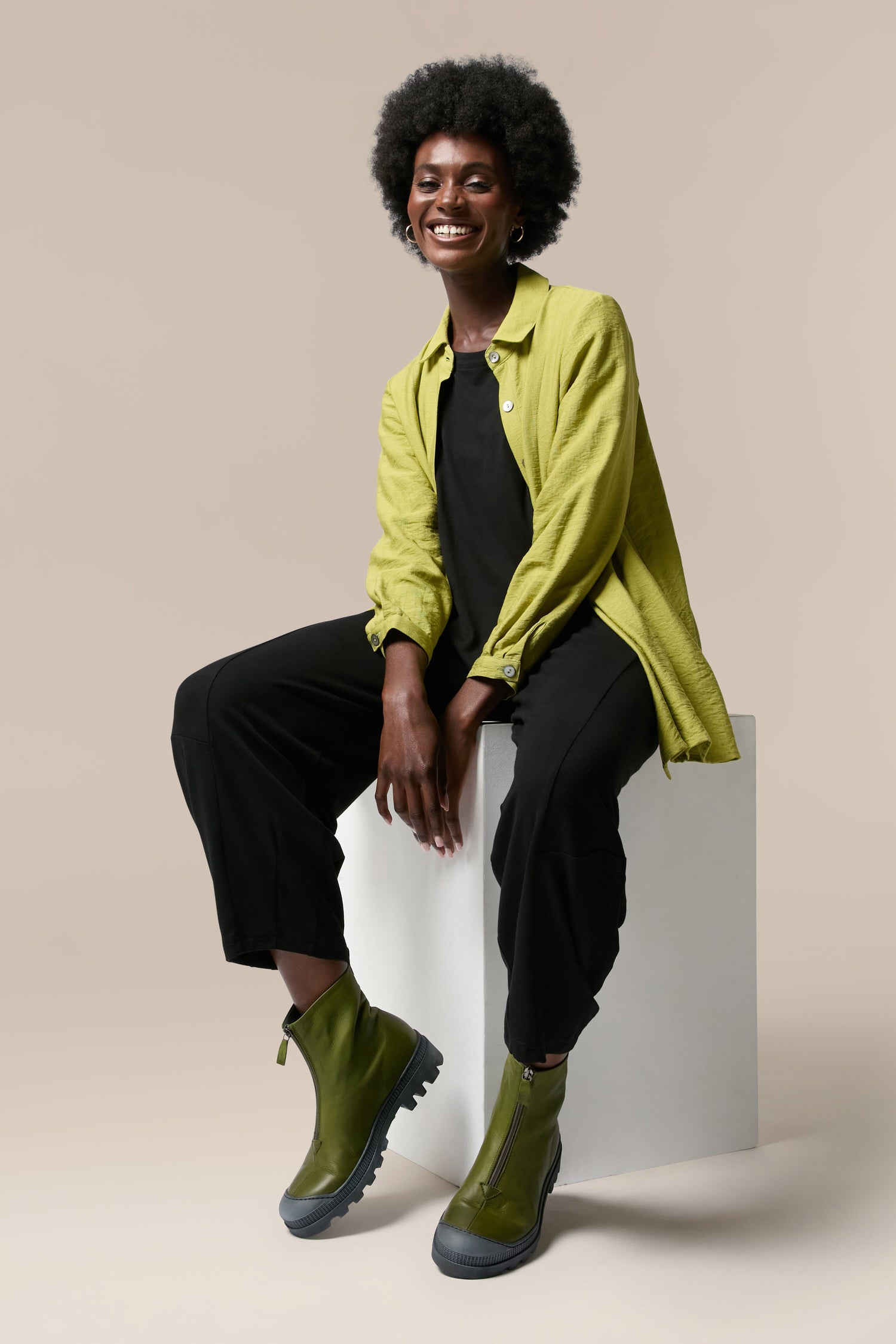 A black woman sitting on a white cube wearing Zip Front Boots.