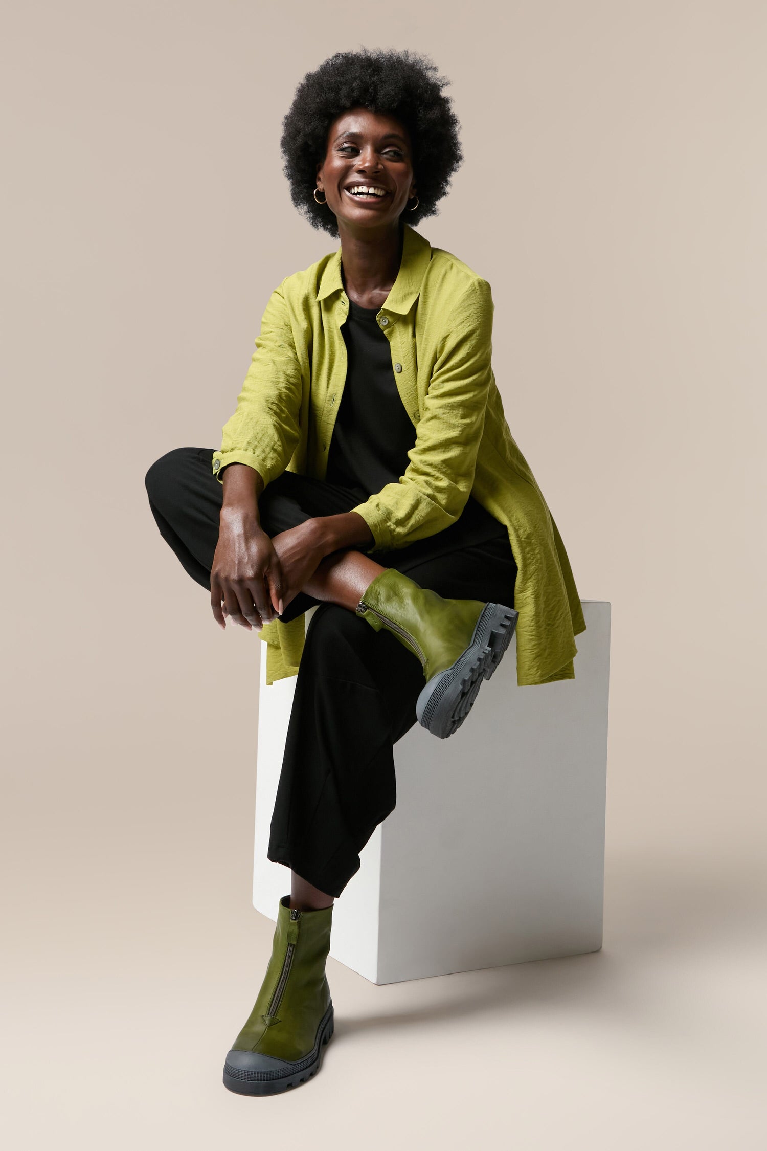 A black woman sitting on a white cube wearing Zip Front Boots.