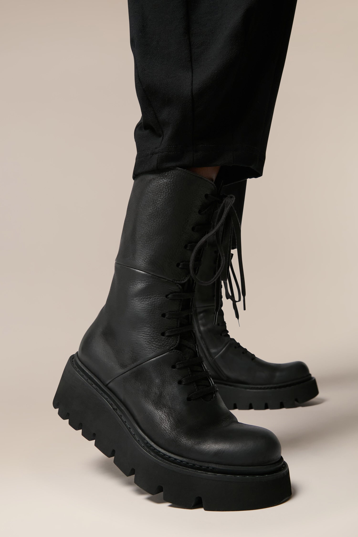 A man wearing black combat boots, showcasing Platform Lace Up Leather Boots with Italian craftsmanship on a grey background.