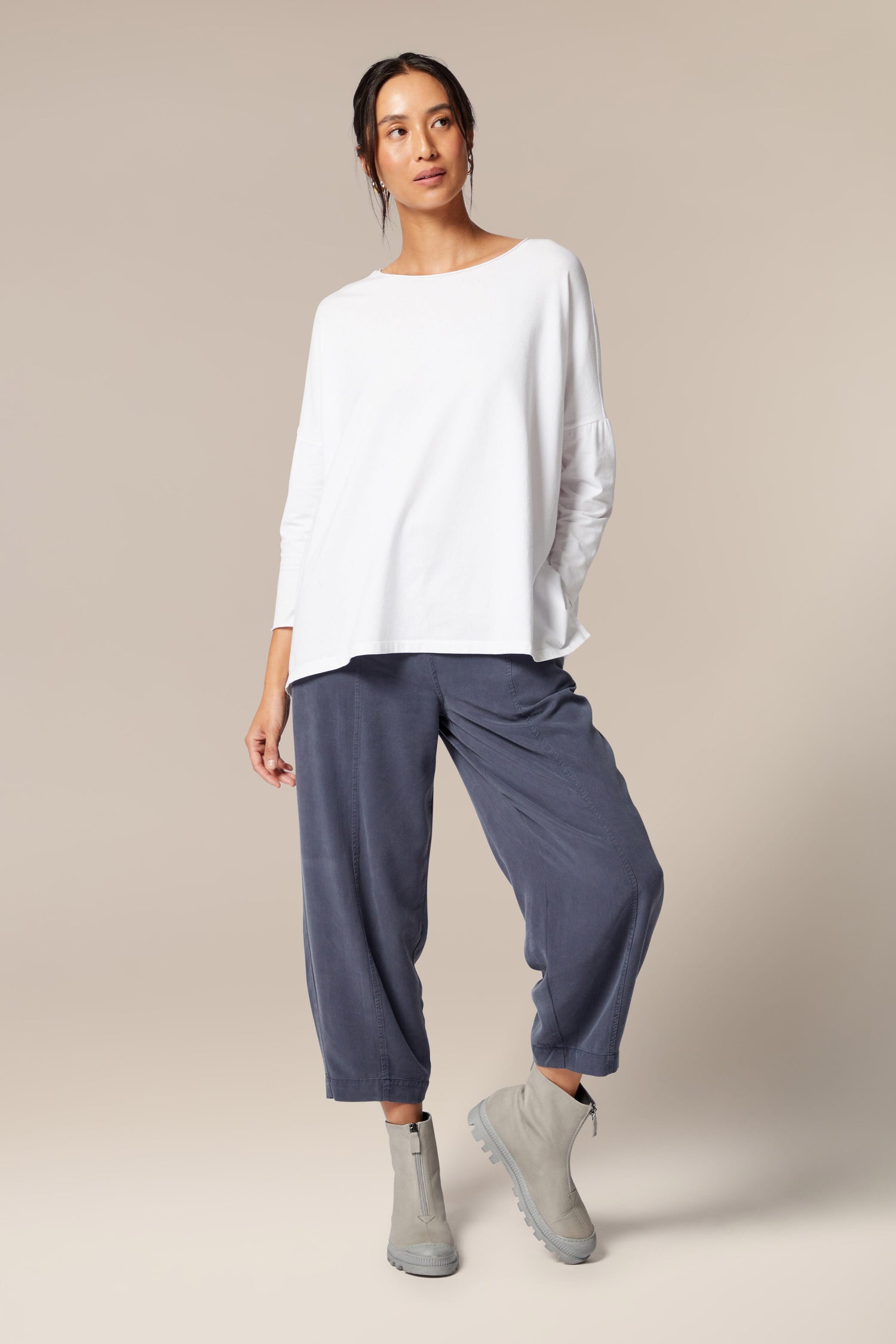 A woman in minimalist style attire, wearing a white t-shirt and blue pants paired with Lofina Zip Front Boots.