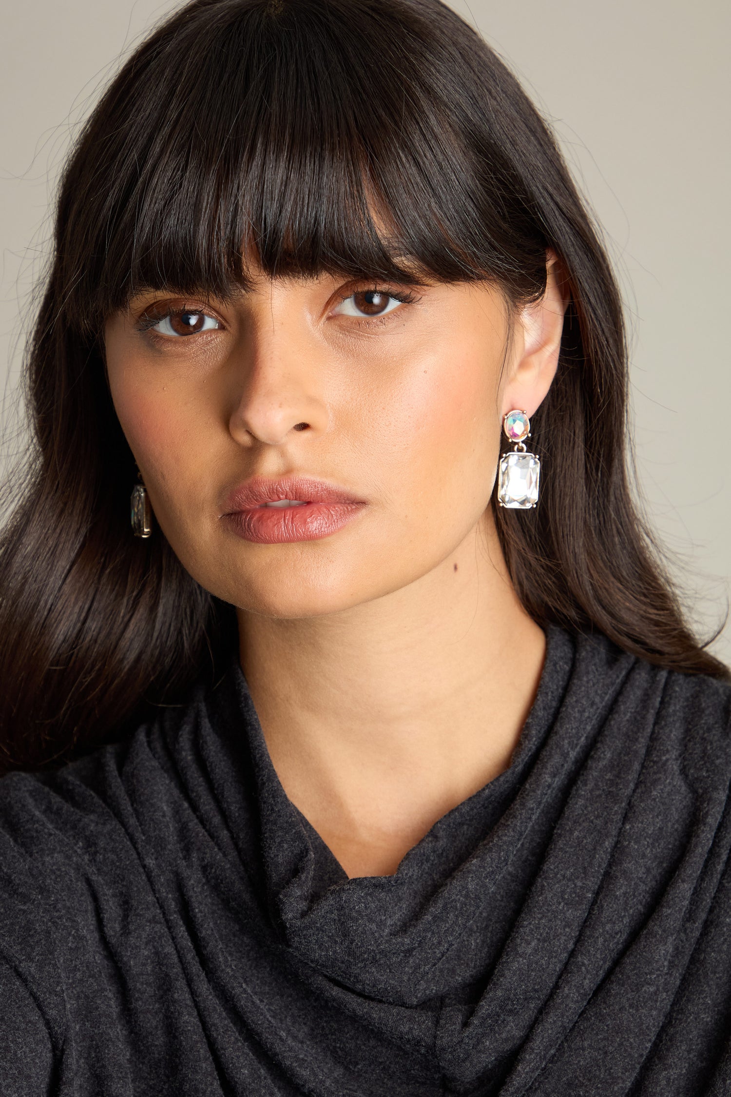 A woman with long dark hair is captured against a plain background, wearing a dark gray top and the exquisite Twin Gemstone Earrings while looking at the camera.