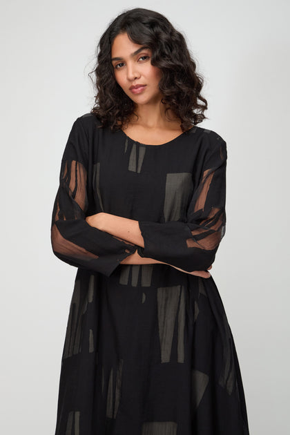 Woman with wavy dark hair, wearing a Cut Out A Line Dress, stands with arms crossed against a plain light background.