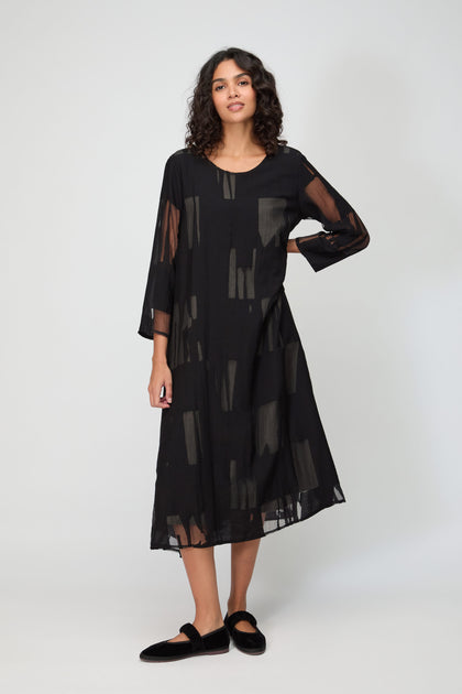 Woman wearing a loose-fitting Cut Out A Line Dress with sheer patterns and black slip-on shoes, standing against a plain light background.