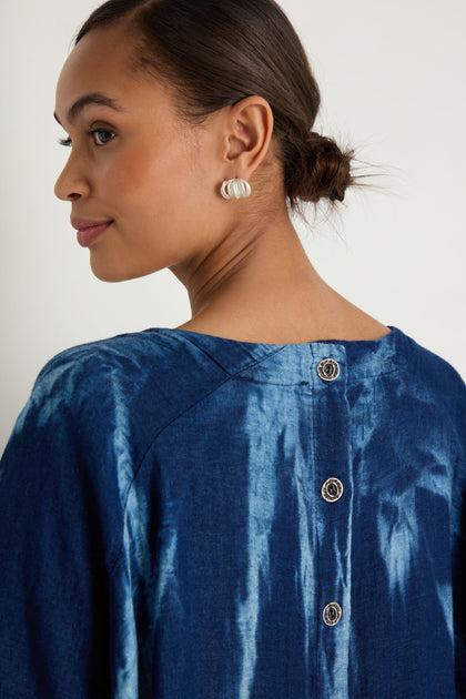 A woman with her hair in a low bun is wearing silver earrings and the Soft Denim Button-Back Tunic, featuring three visible buttons down the back.