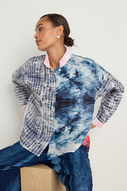 A woman wearing the Floral Back Easy Shirt, featuring contrasting blue and white designs, sits on a wooden block and looks to the side.
