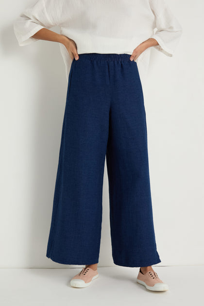 Person wearing a white top, Wide Leg Slit Trousers with an elastic waistband, and light pink sneakers, standing against a plain white background.