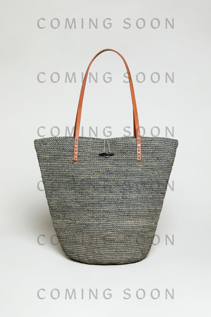 The Ilana Raffia Basket, a large woven gray tote with brown leather handles, is shown on a plain light background with "COMING SOON" displayed over the image.