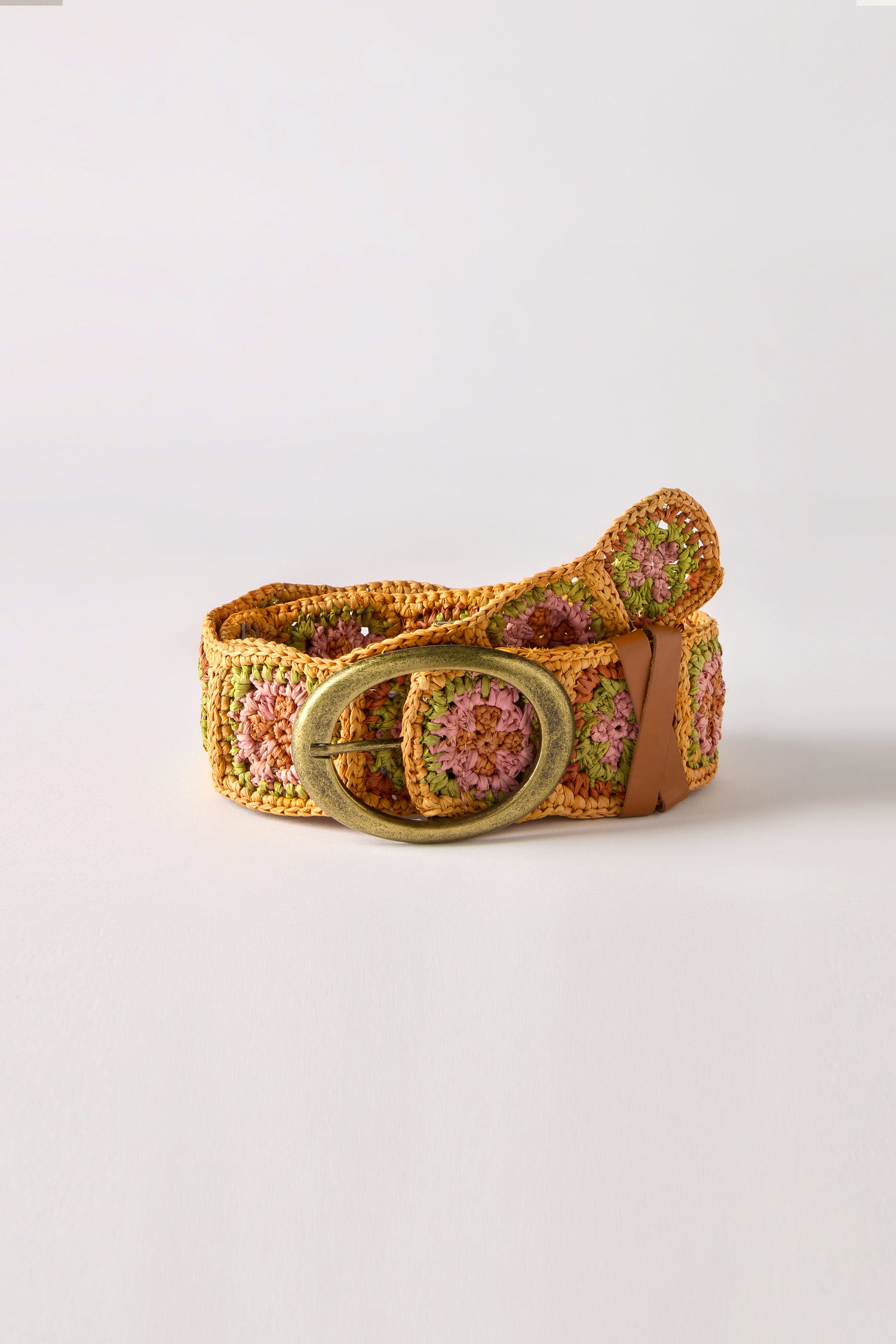 The Cinzoa Raffia Belt showcases a large round metal buckle and a pink and green floral pattern on a beige background, displayed on white. It's the perfect versatile accessory to elevate any outfit with its boho-chic charm.