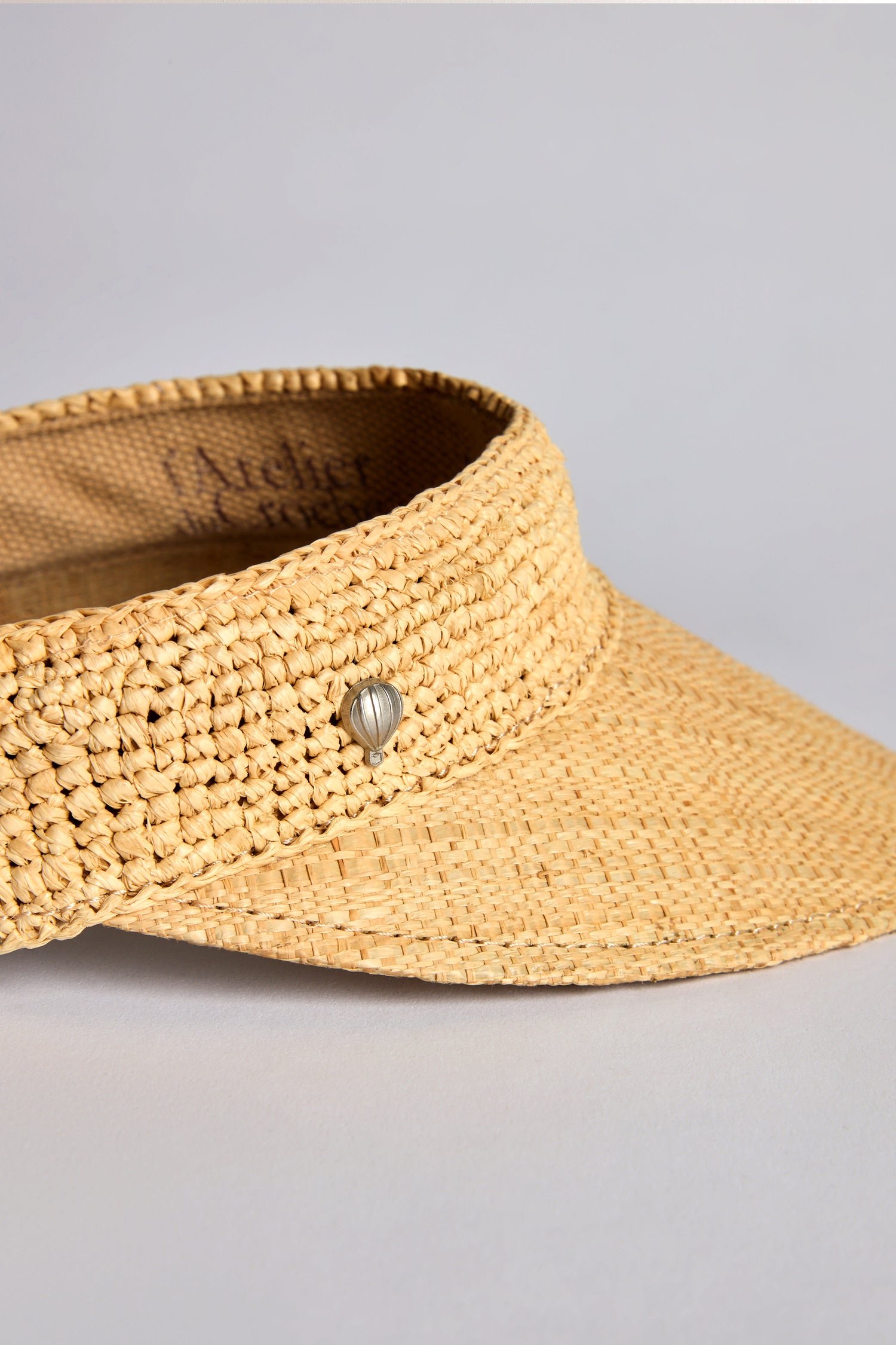 The Garossoa Visor, a woven straw marvel, is adorned with a stylish metallic heart on its band. It offers excellent sun protection while embodying the spirit of Le Voyage en Panier against tranquil settings.