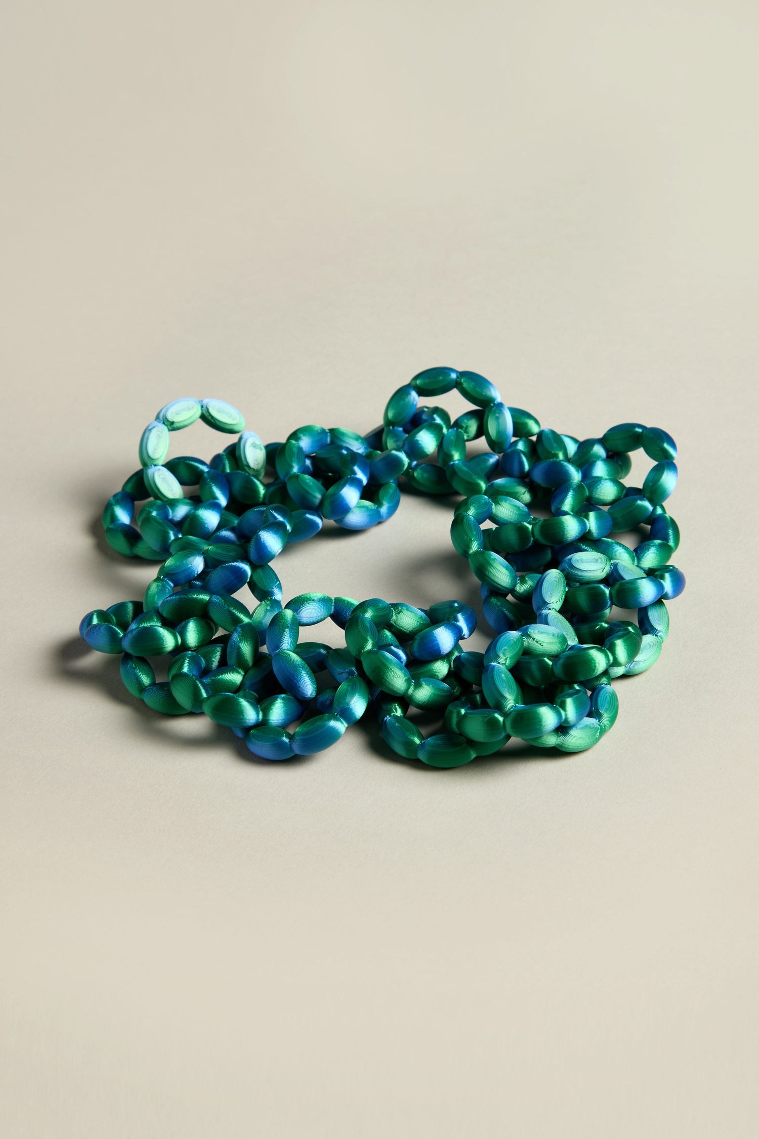 A 3D Printed Links Necklace featuring green and blue interlocking chain links is set against a neutral background. Its ultra-lightweight design reflects the innovative style of Maison 203.