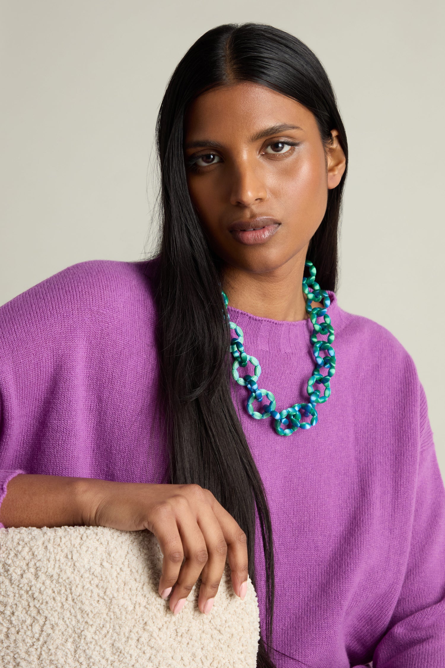 A person with long black hair wears a purple sweater and a 3D Printed Links Necklace by Maison 203, resting their hand on a textured surface.