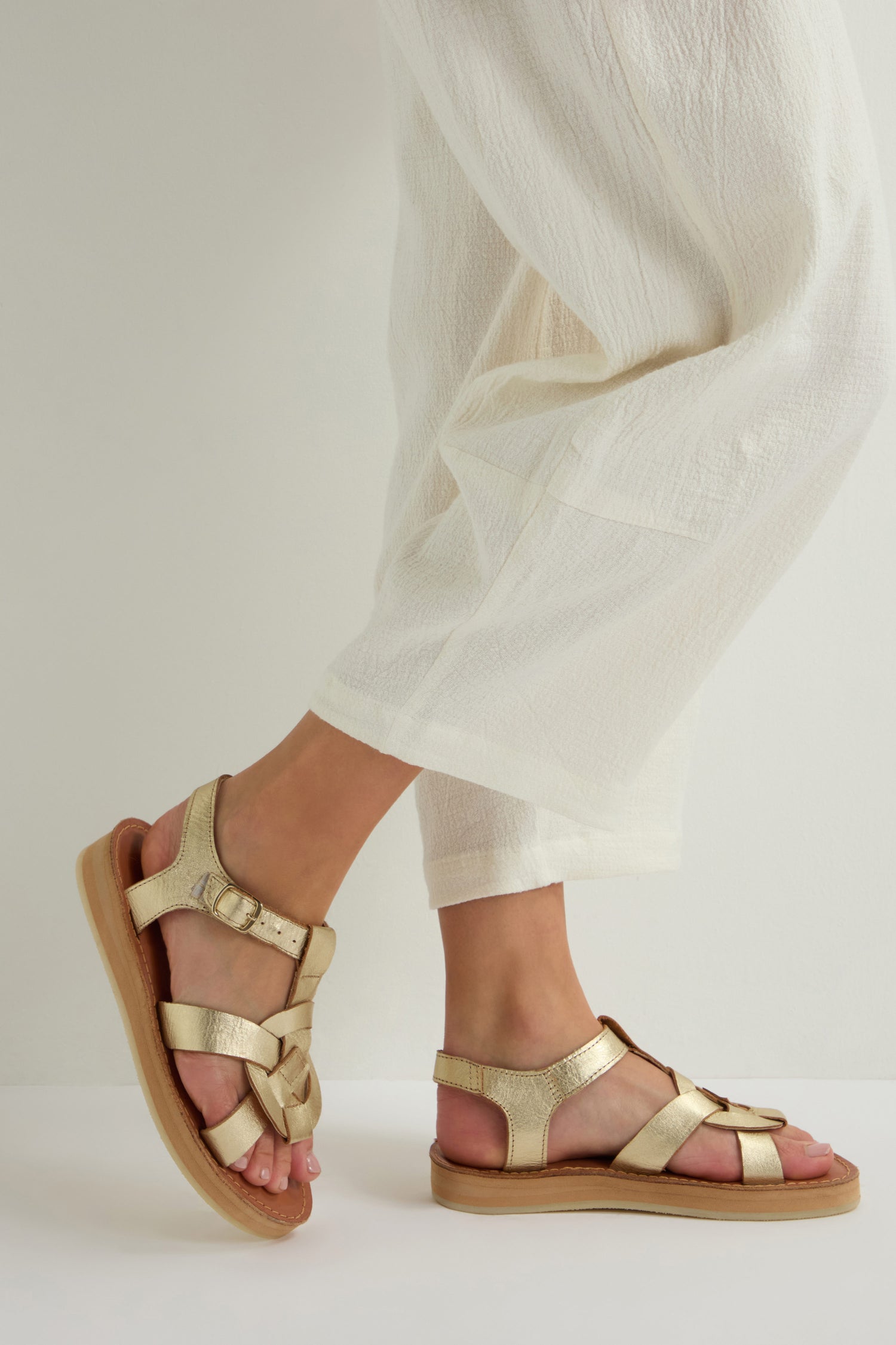A person in cream-colored pants and Tulum Leather Buckle Sandals, made from premium handmade leather, stands on a light surface.