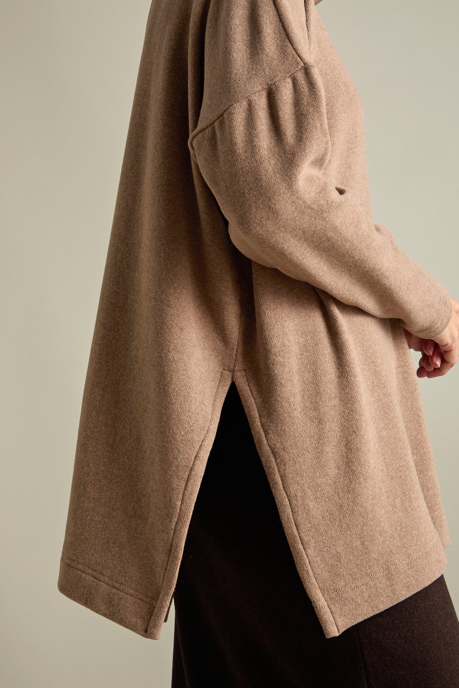 Side view of a person wearing a loose-fitting Zeppola Rib Neck Soft Jersey Tunic with a side slit and dark-colored bottoms, standing against a neutral background. The high neckline and cosy fleece fabric add to the outfit's comfort and style.