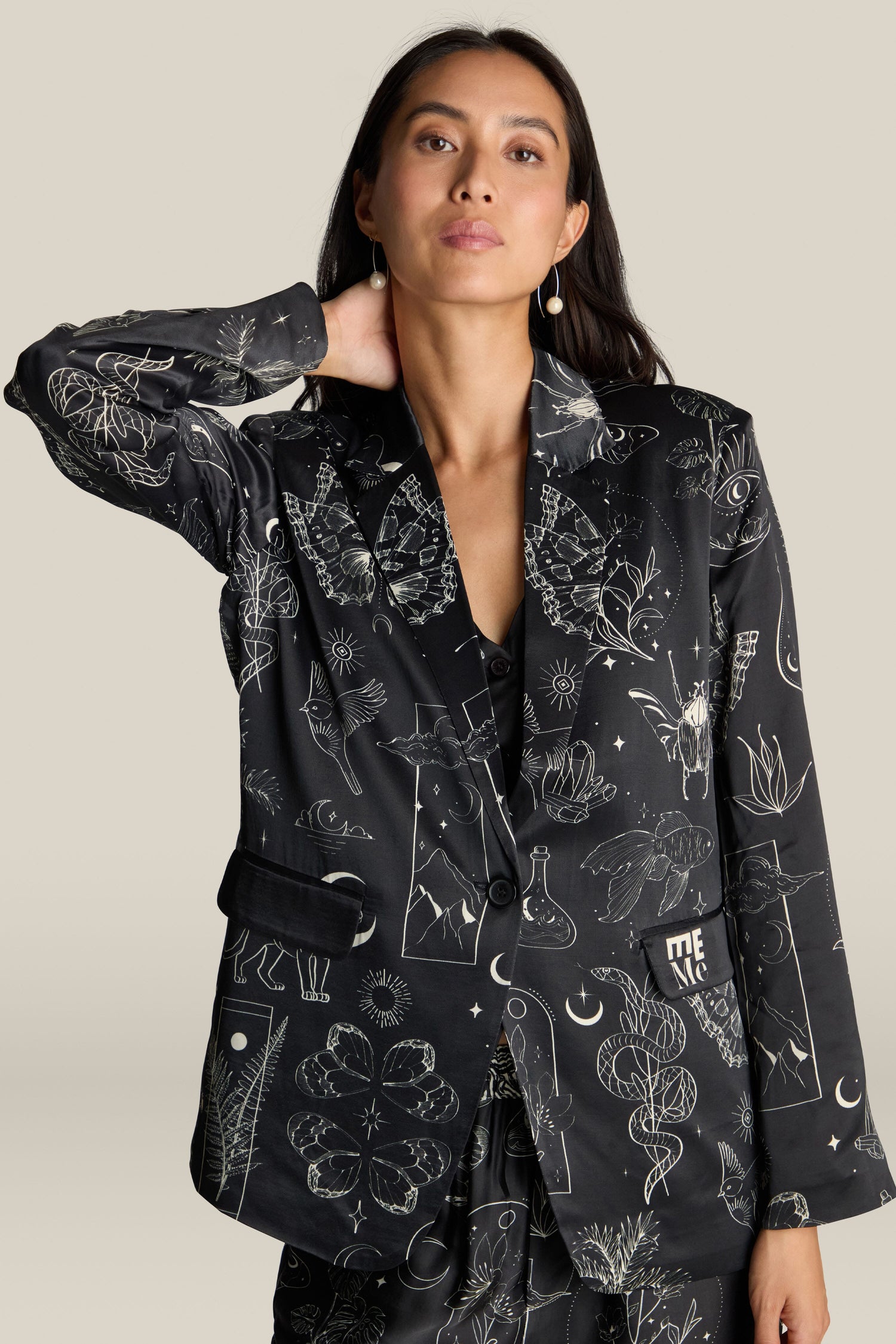 A woman wearing the Molly Printed Jacket, a luxurious black blazer made of viscose and rayon adorned with intricate white line art designs, stands against a plain background.