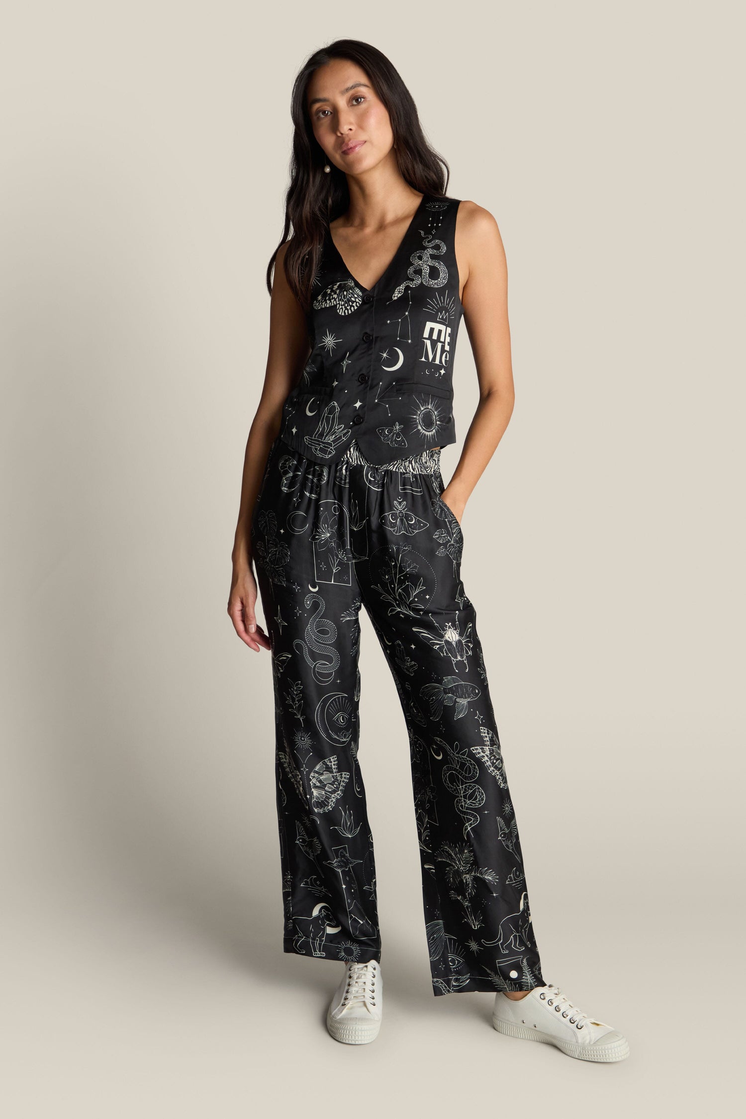 A woman stands against a neutral background wearing the Cameron Vest and matching wide-leg pants with a mystical digital print, paired with white sneakers.