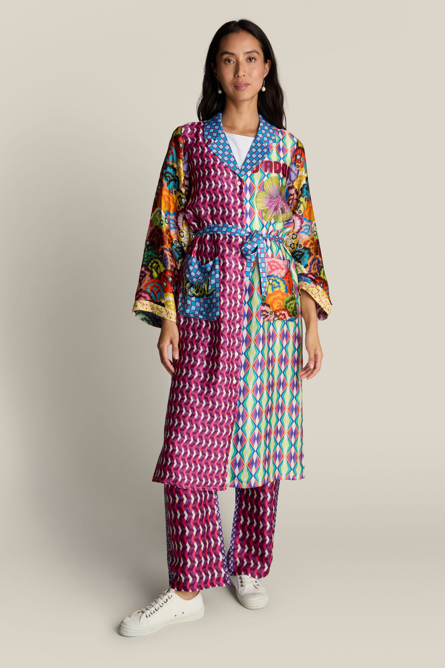 A person wearing the Nova Kimono, adorned in a vibrant patchwork design showcasing an array of lively patterns and textures, stands against a plain background. The ensemble is completed with matching pants, further enriched by delicate tiger illustrations that add a subtle touch of wildness to the eclectic outfit.