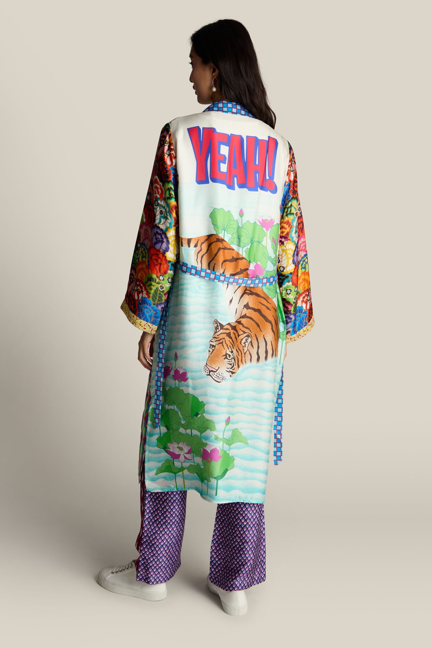 A person is standing, facing away, adorned in a ME369 Nova Kimono that boasts vibrant, eclectic patterns with a striking "YEAH!" on the back, along with majestic tiger illustrations and floral motifs in an array of colorful designs.