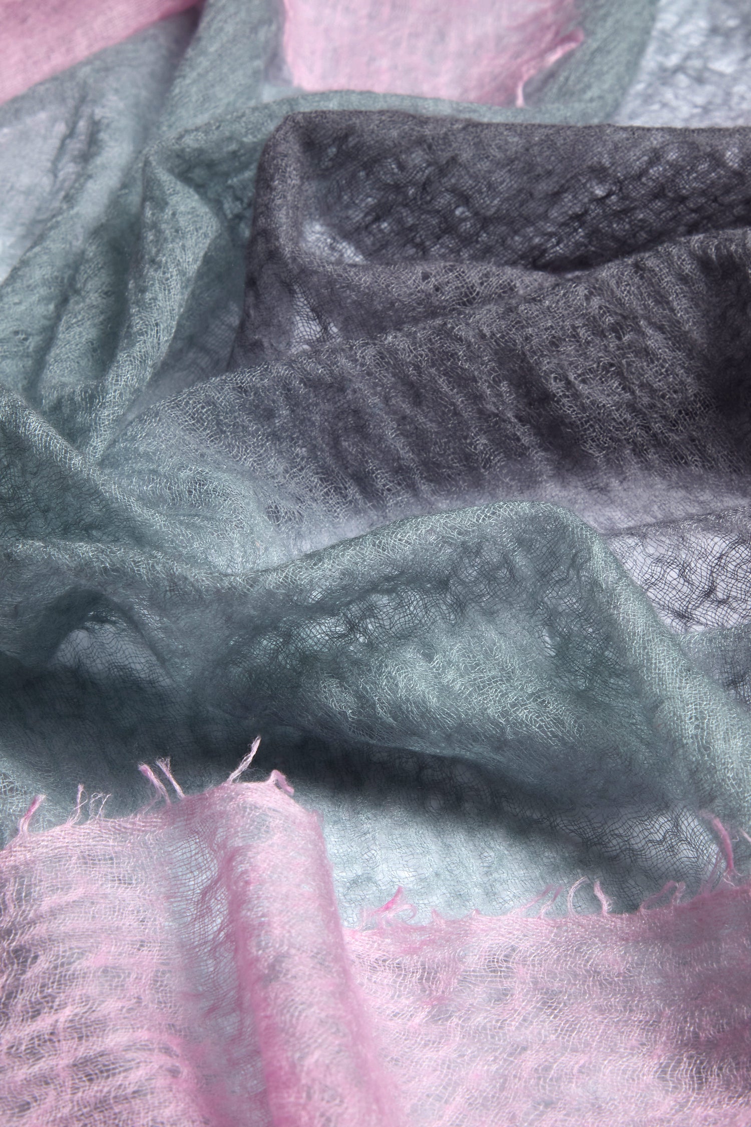 The close-up shows a textured pastel pattern in light blue, pink, and gray on sheer fabric. This exquisite design belongs to the St Tropez Cashmere Shawl, a handcrafted piece ethically made in Nepal.