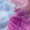 Close-up of a person wearing a pink jacket, with only part of their face and shoulder visible. Draped elegantly is a luxurious St Tropez Cashmere Shawl. The background appears blurred with a mix of blue tones, resembling a gradient watercolour design.