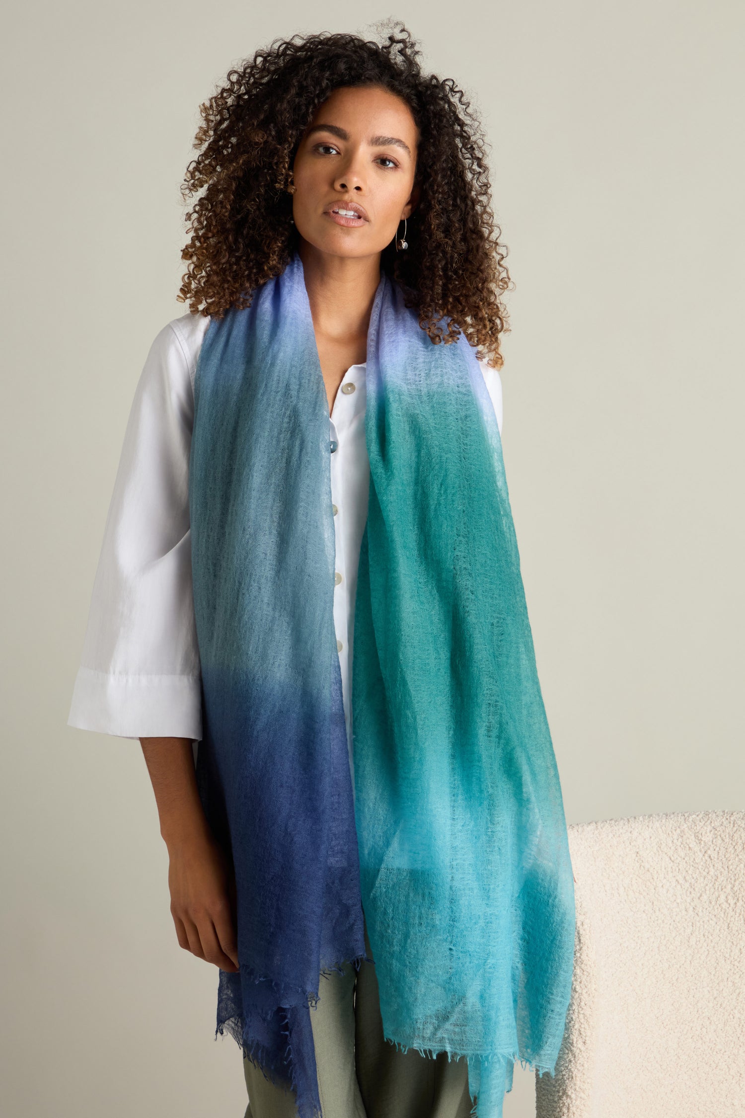 A person wearing a white shirt and a St Tropez Cashmere Shawl, featuring a blue-to-green gradient watercolor design, stands in front of a plain background.