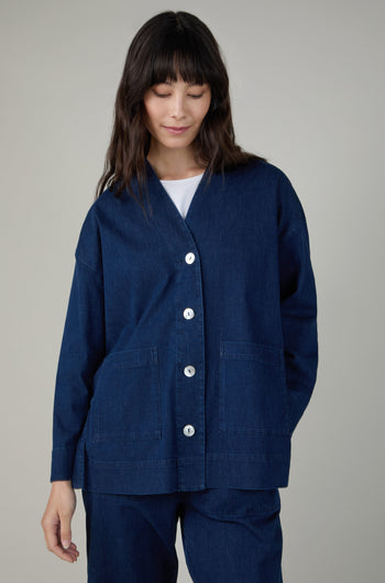 A person wears the Stretch Denim Boxy Jacket in dark blue with large front pockets and matching pants, standing against a plain light background.