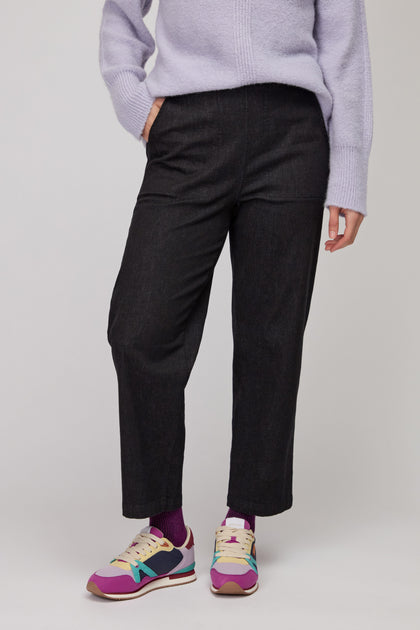 Person wearing a light purple sweater, Black Stretch Denim Straight Trousers, colorful sneakers, and purple socks, standing against a plain background.