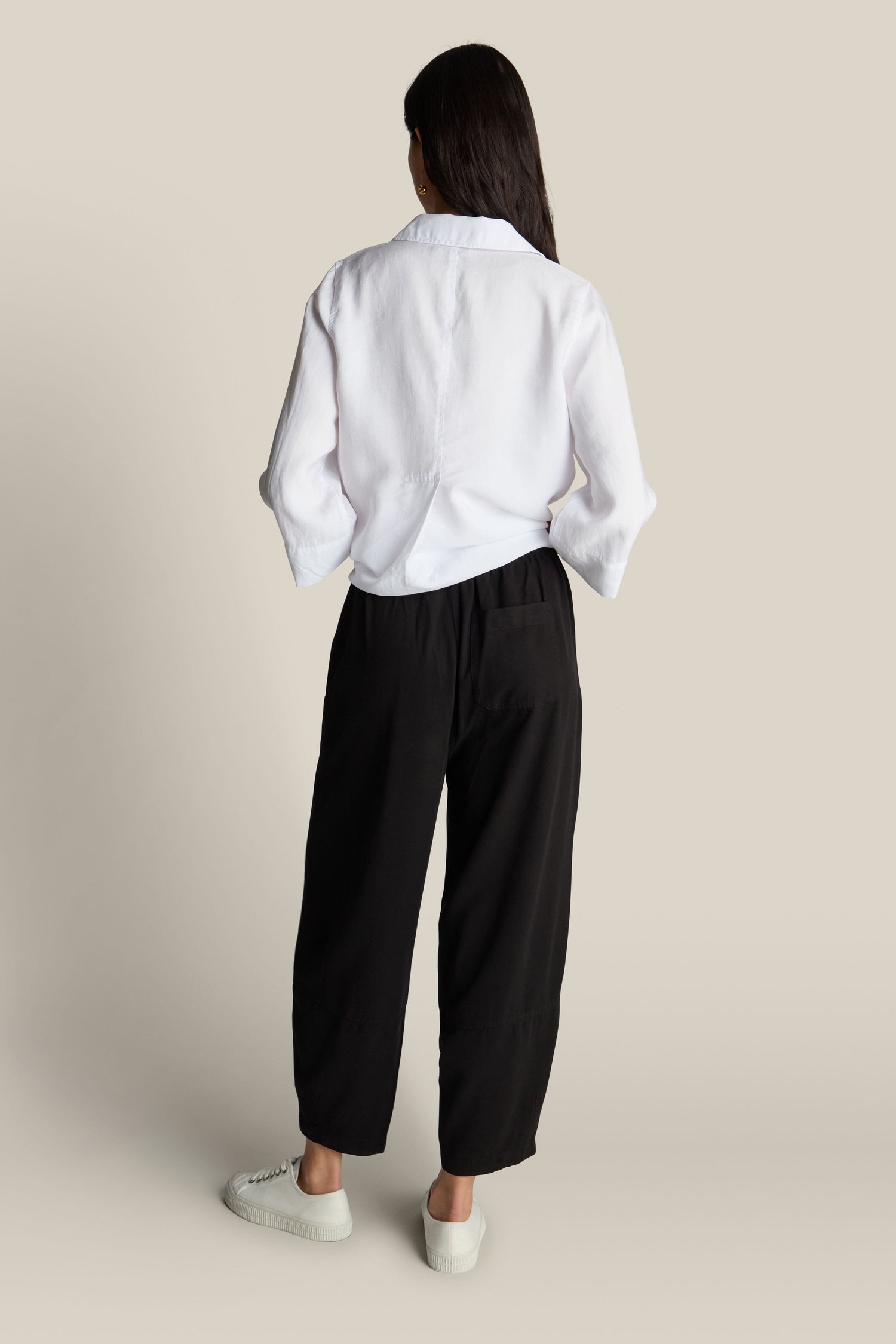 A person stands with their back turned, dressed in a white long-sleeve shirt and Fluid Twill Bubble Trouser featuring an elasticated waist, paired with white sneakers, against a neutral background.