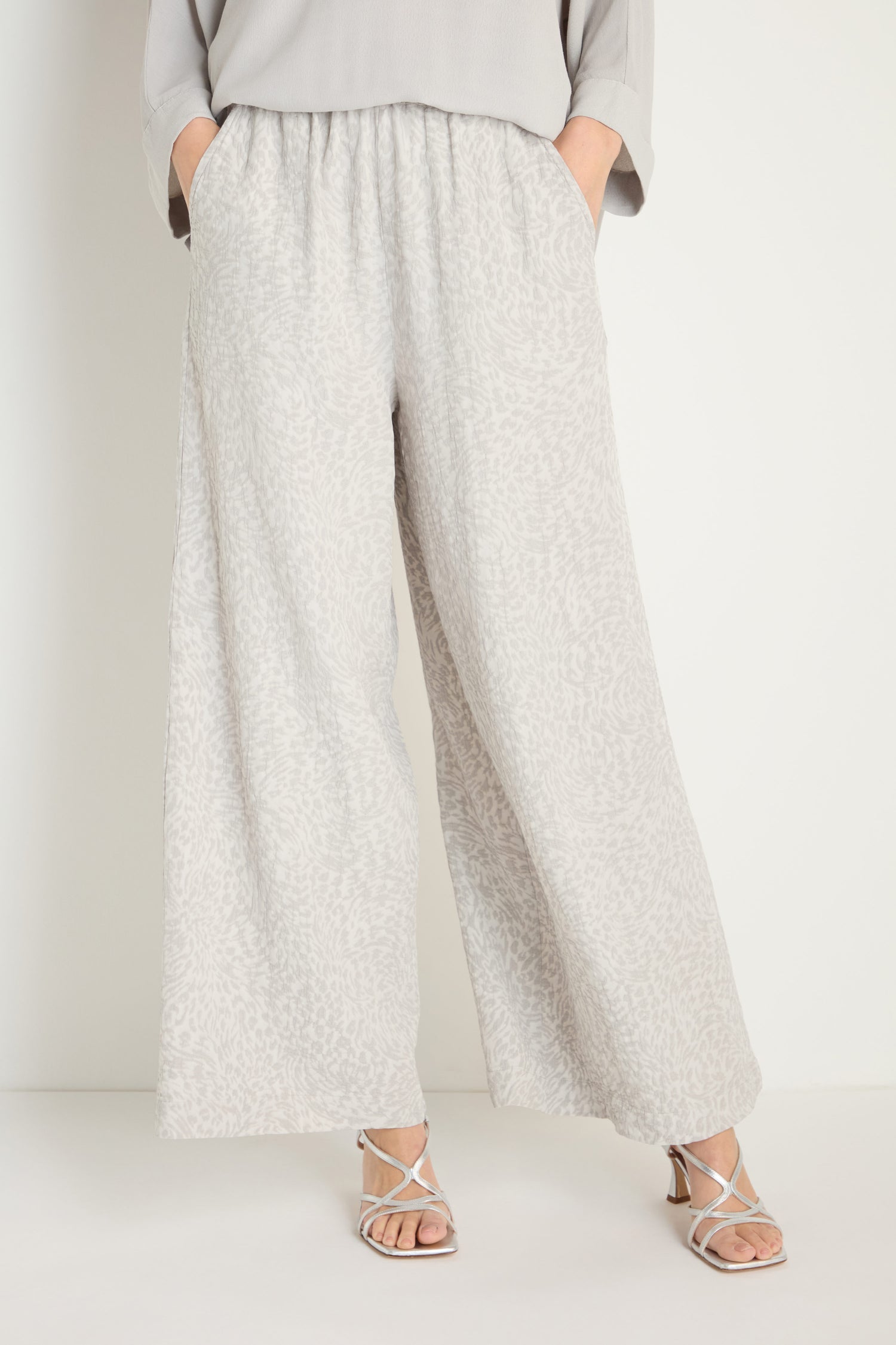 Wearing Animal Textured Jacquard Wide Trouser in light gray, a matching top, and white sandals, a person stands with hands in pockets against a plain background.