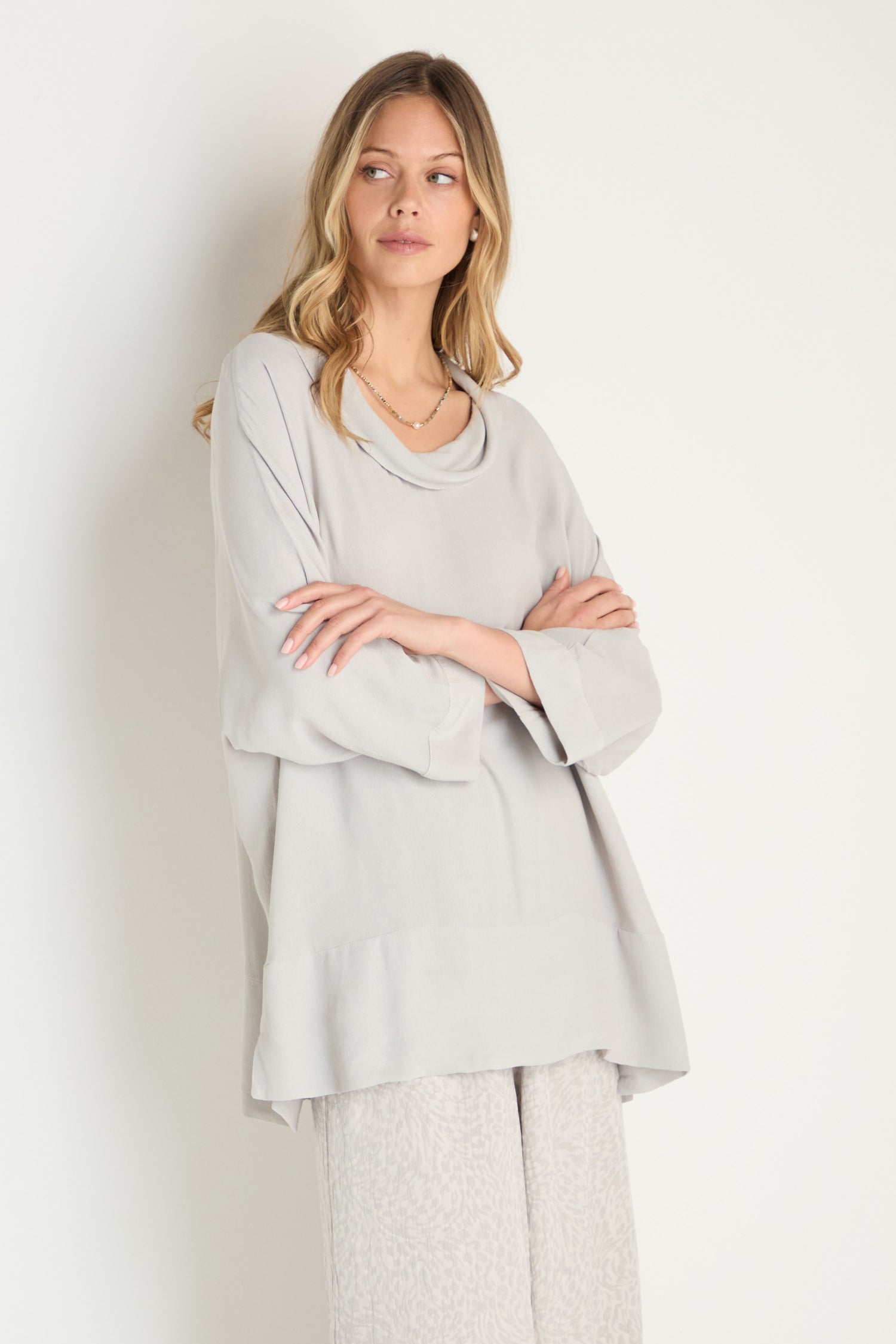 A woman with long, wavy blonde hair wears the Crepe Boxy Top in light gray and patterned light gray pants, standing against a plain white background.