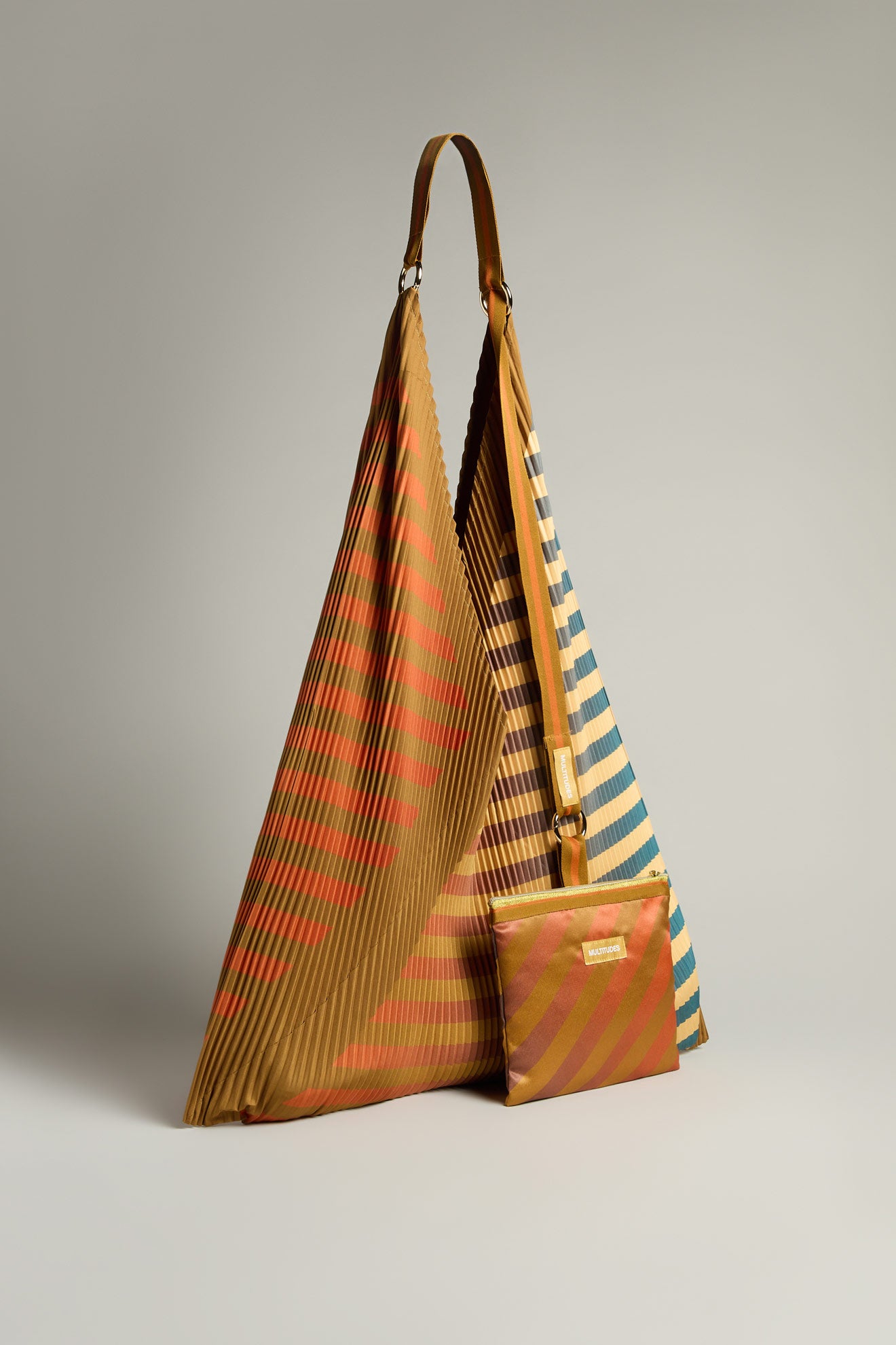 The Pleated Y Handbag is a large, eco-friendly triangular bag with orange and blue stripes, paired with a matching smaller pouch, all set against a neutral background.